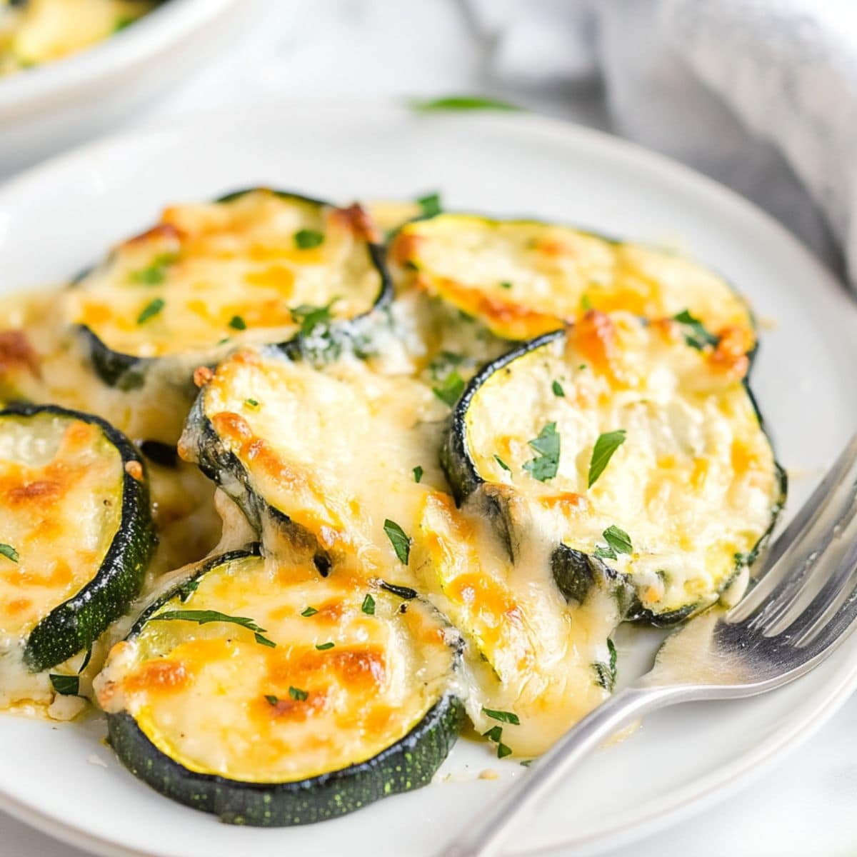 Serving of cheesy scalloped zucchini on a white plate.