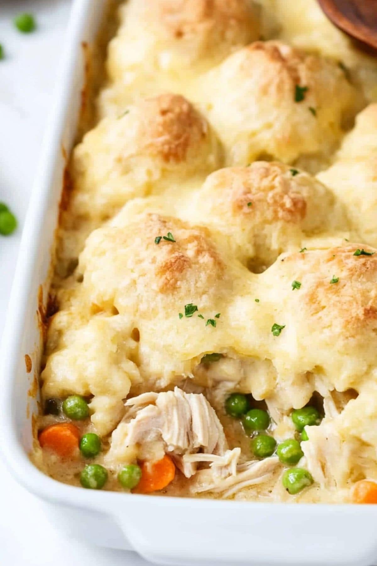 Chicken and dumplings with shredded chicken, carrots and peas in a creamy sauce in a baking dish.