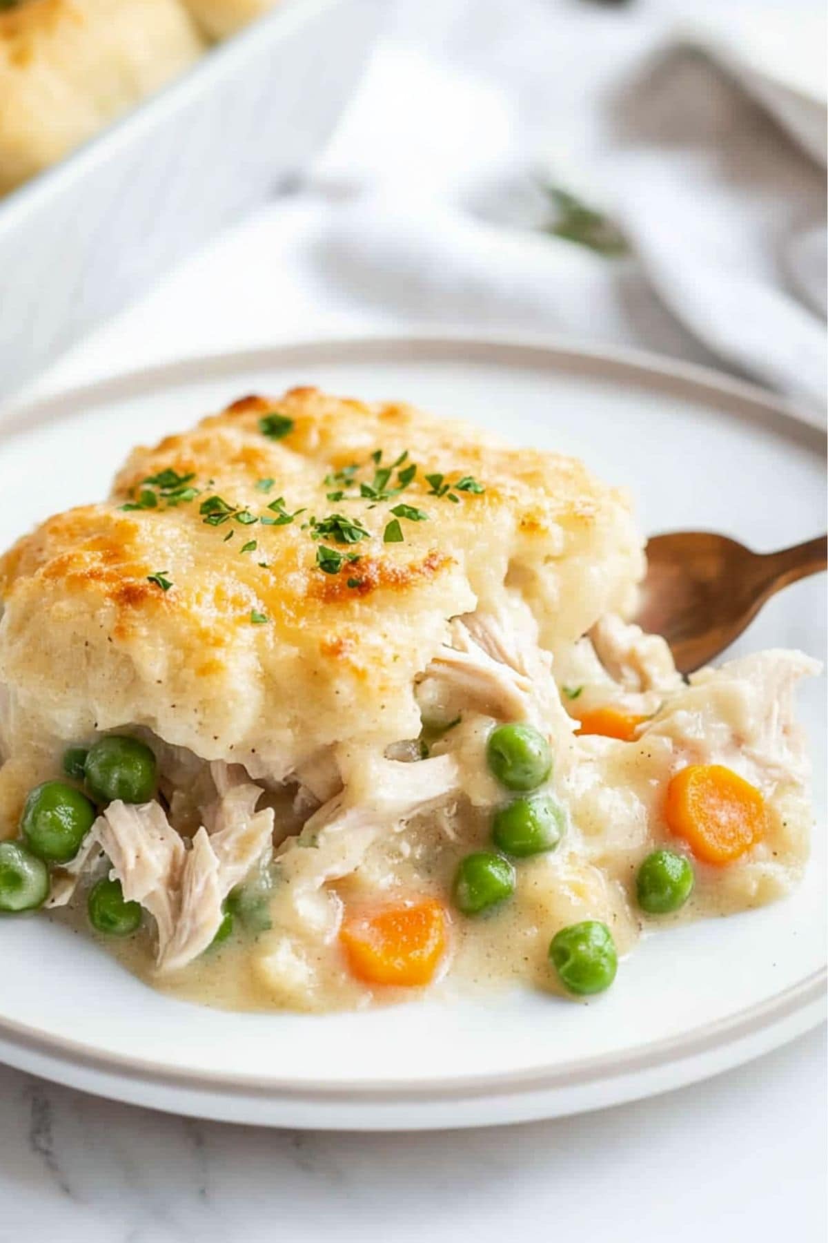 Serving of creamy chicken and dumplings casserole with green peas, carrots and shredded chicken served on a white plate.