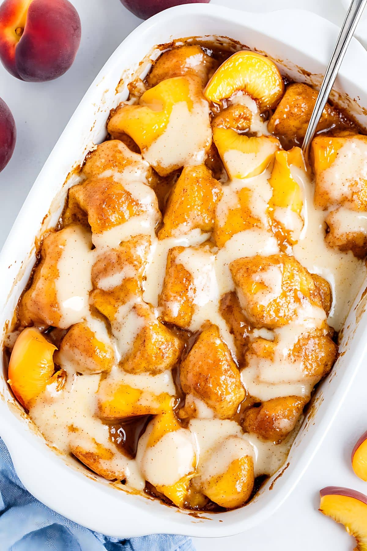 Cinnamon Roll Peach Cobbler in a casserole dish with vanilla icing, top view