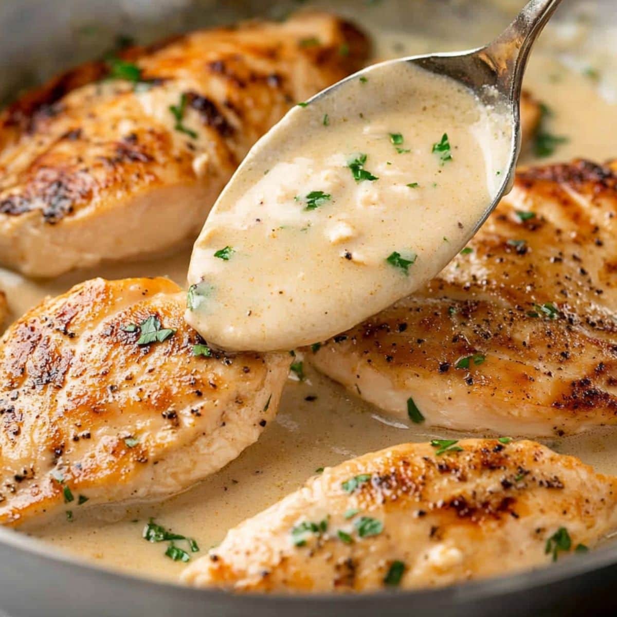 Spoon with a scoop of cream cheese sauce pouring over seared chicken breast.