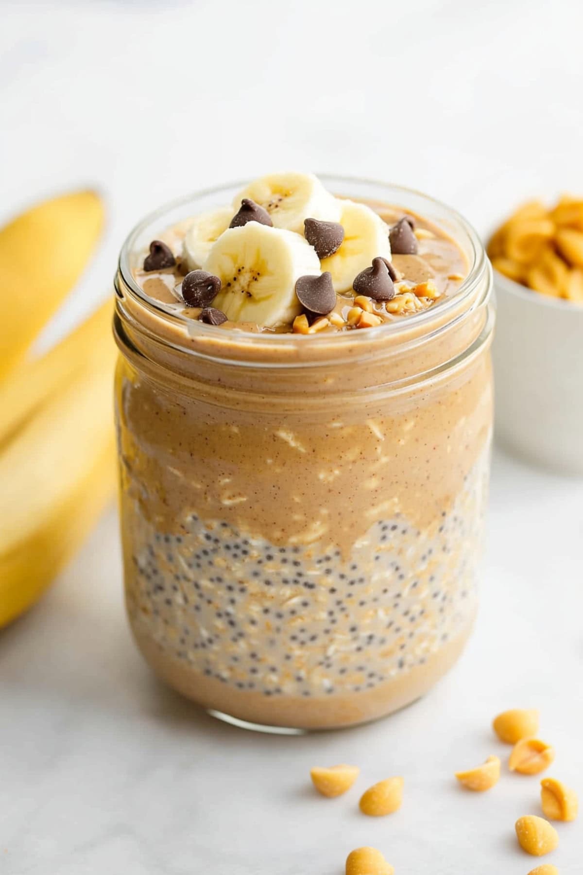 Peanut butter overnight oats in a glass jar with chia seeds, topped with banana slices and chocolate chips.