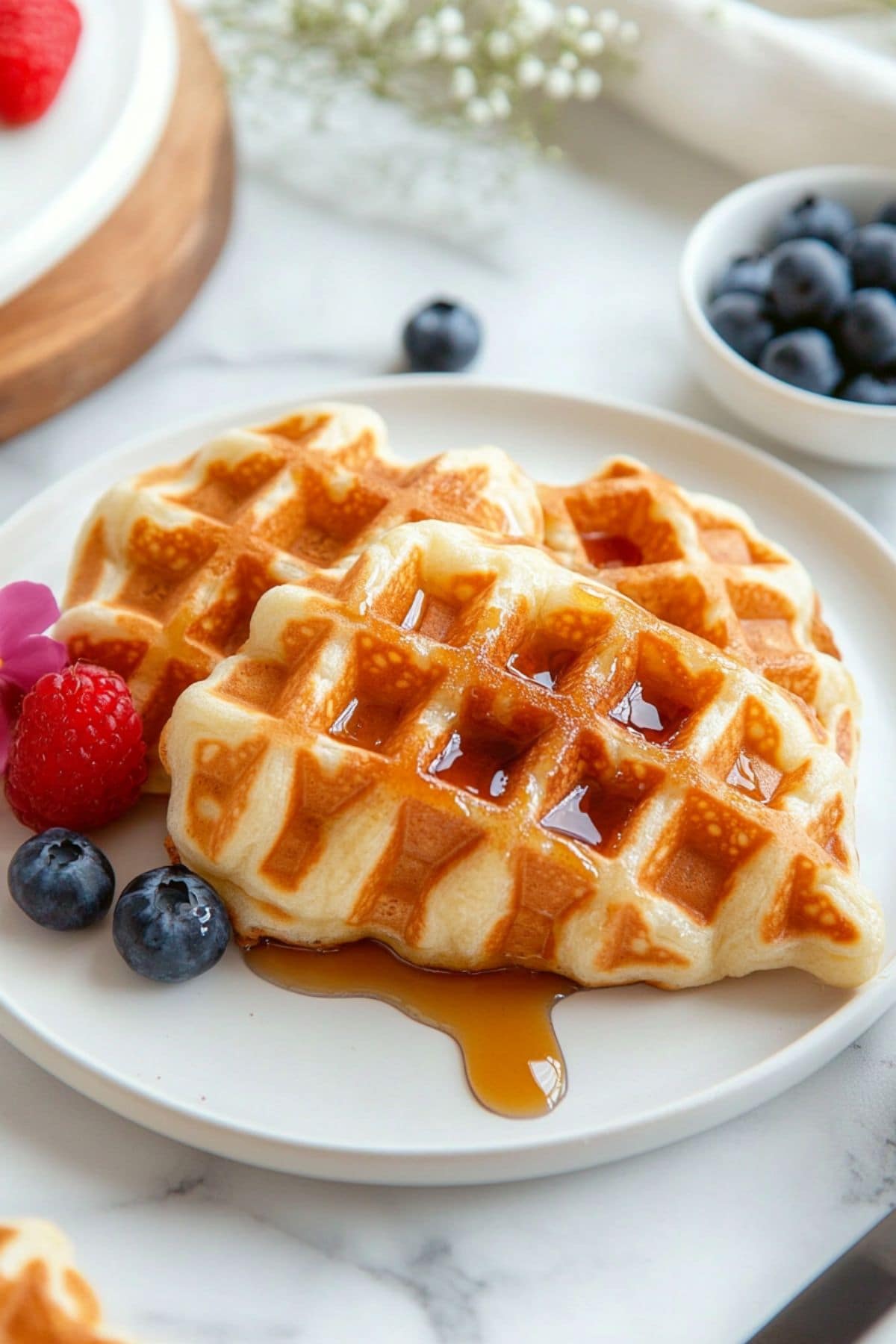 Croissant waffles drizzled with maple syrup garnished with berries served on a white plate.