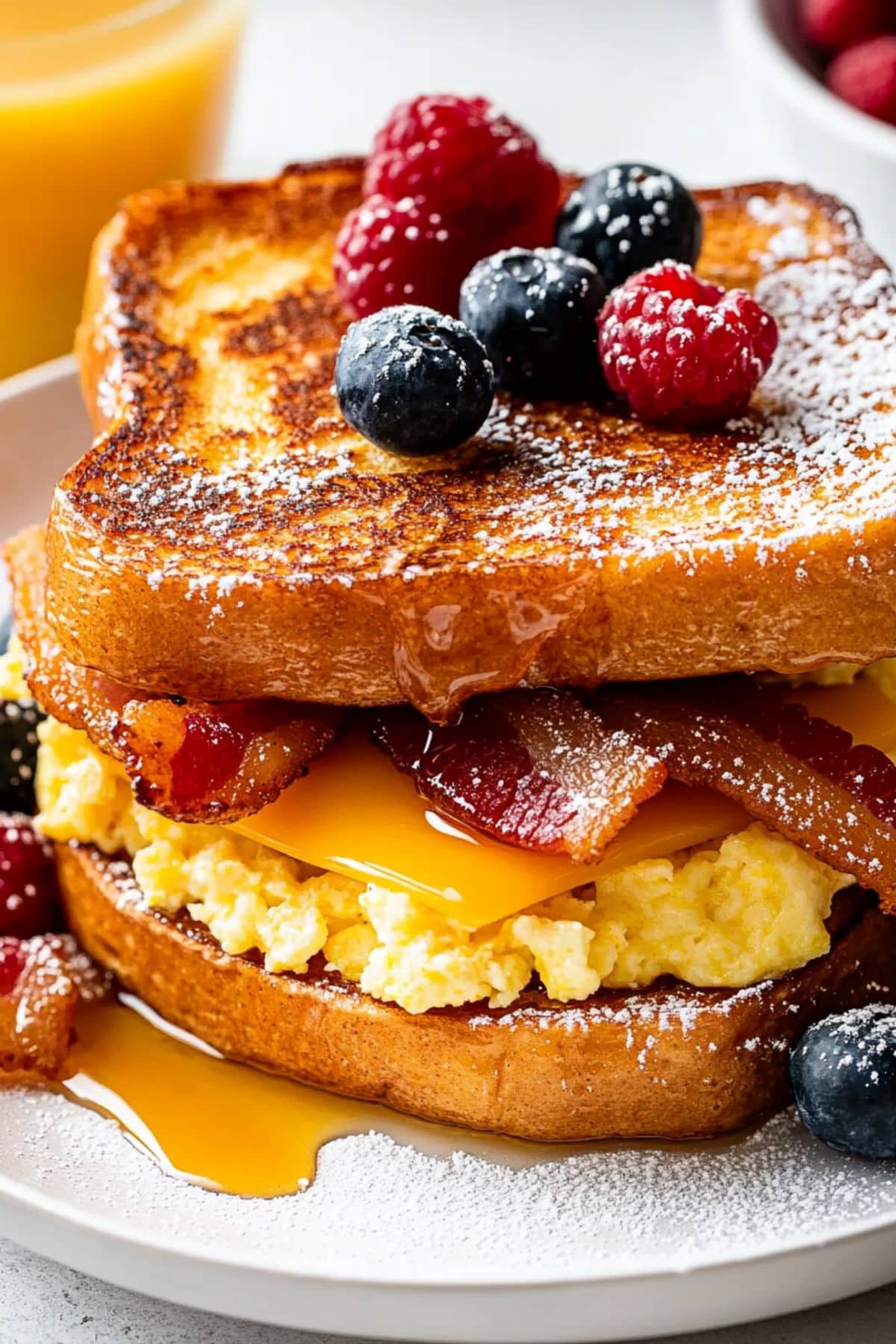 French toast breakfast sandwich with scrambled eggs, bacon and cheese, garnished with syrup and berries.