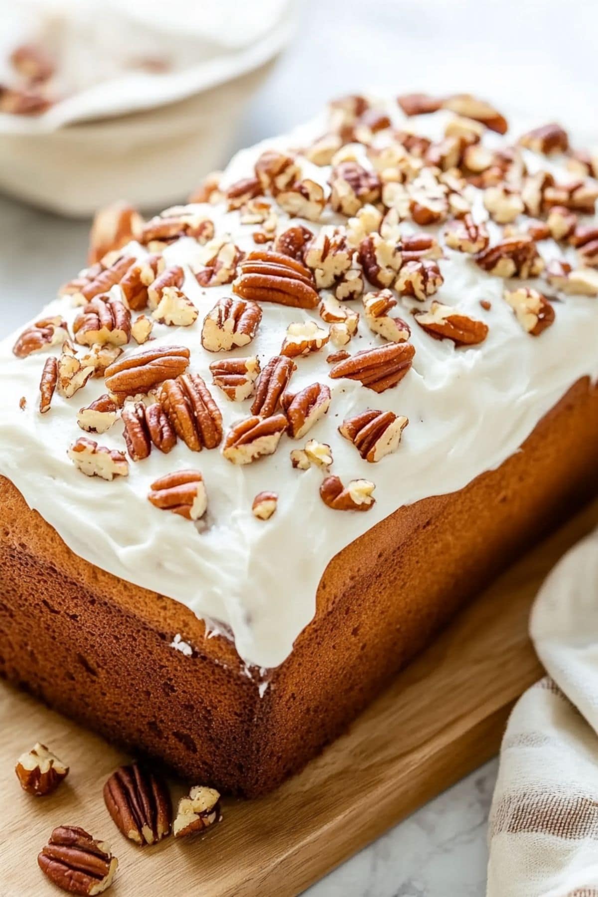 Loaf bread covered with frosting garnished with chopped pecans sitting on a wooden board.