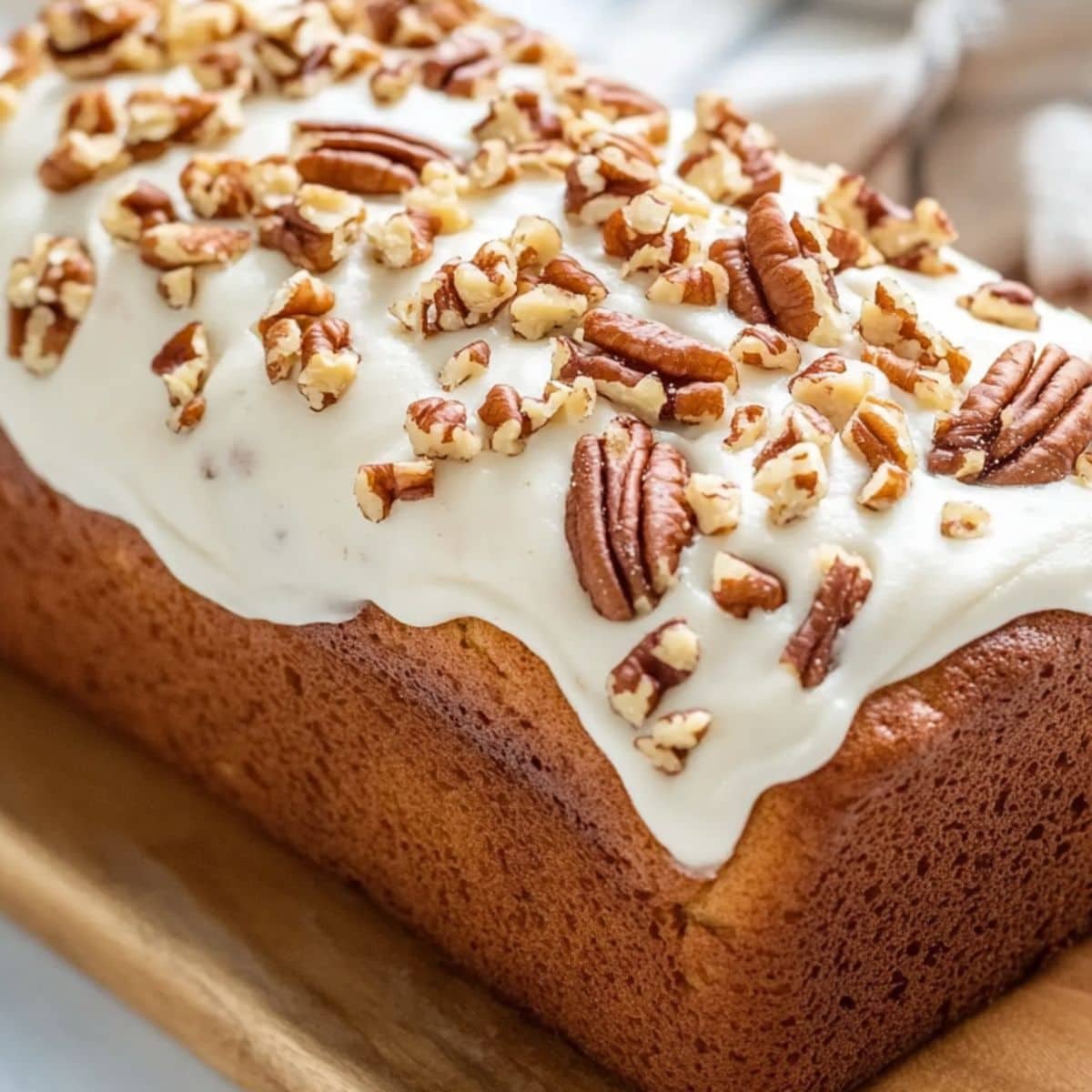 Frosting covered loaf bread on a wooden board garnished with chopped pecans.