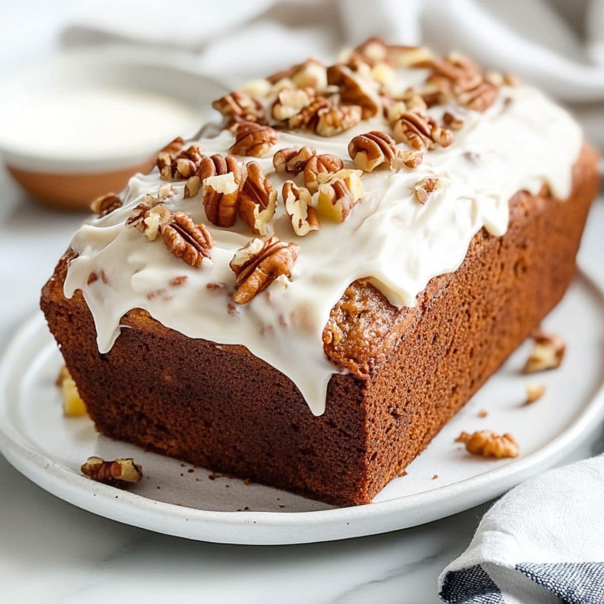 Hummingbird bread with cream cheese frosting garnished with chopped pecans .