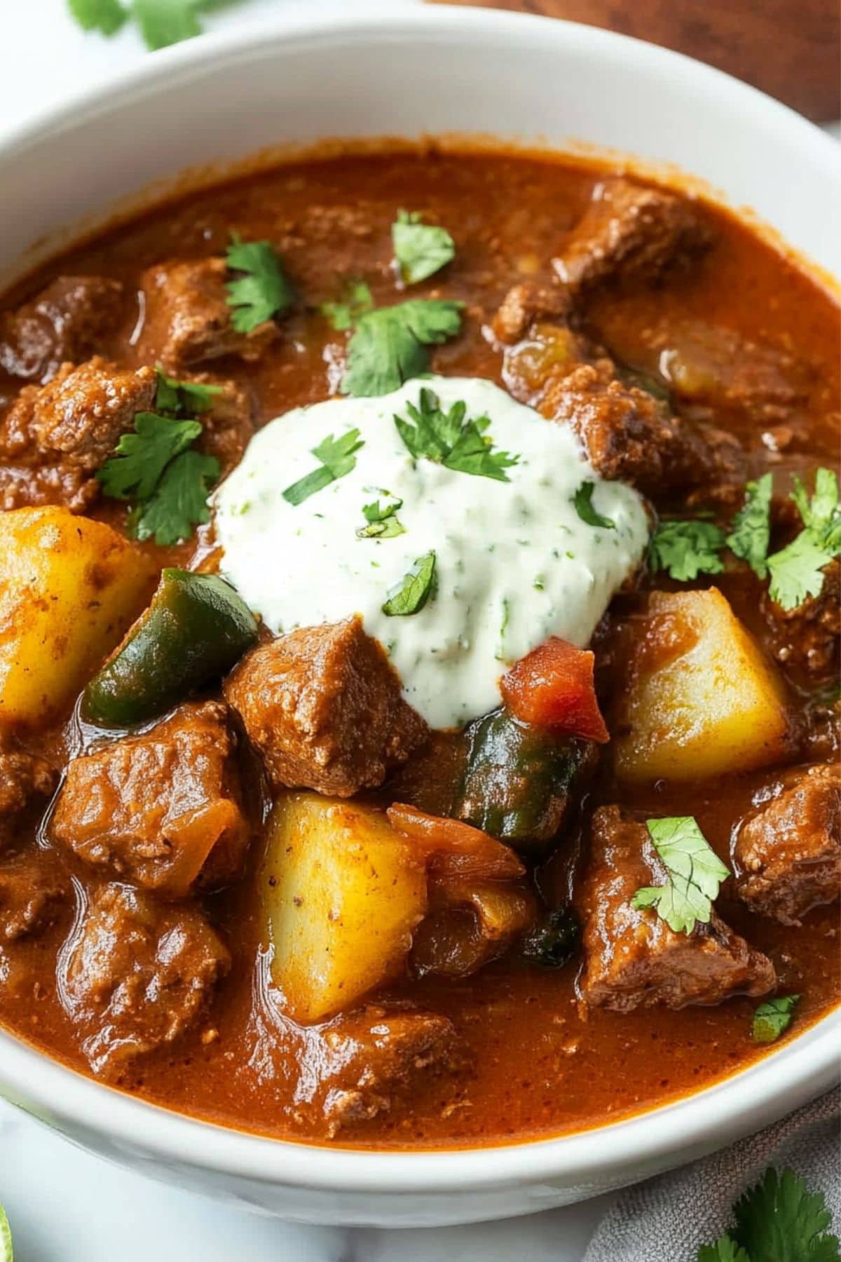 Mexican beef stew served in a white bowl garnished with lime crema.