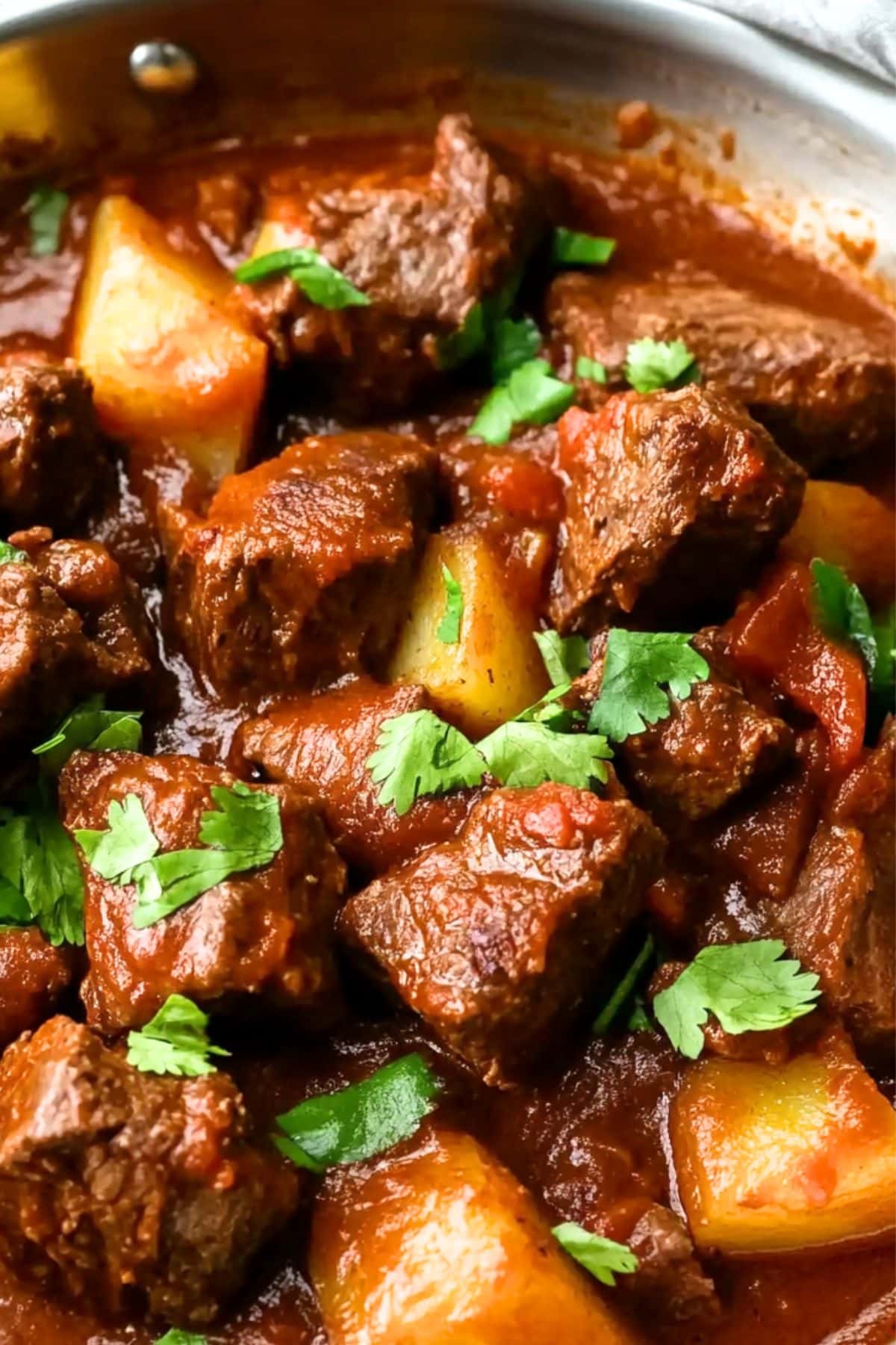 Beef chunks and potatoes cooked in  savory tomatoes sauce in a skillet pan.