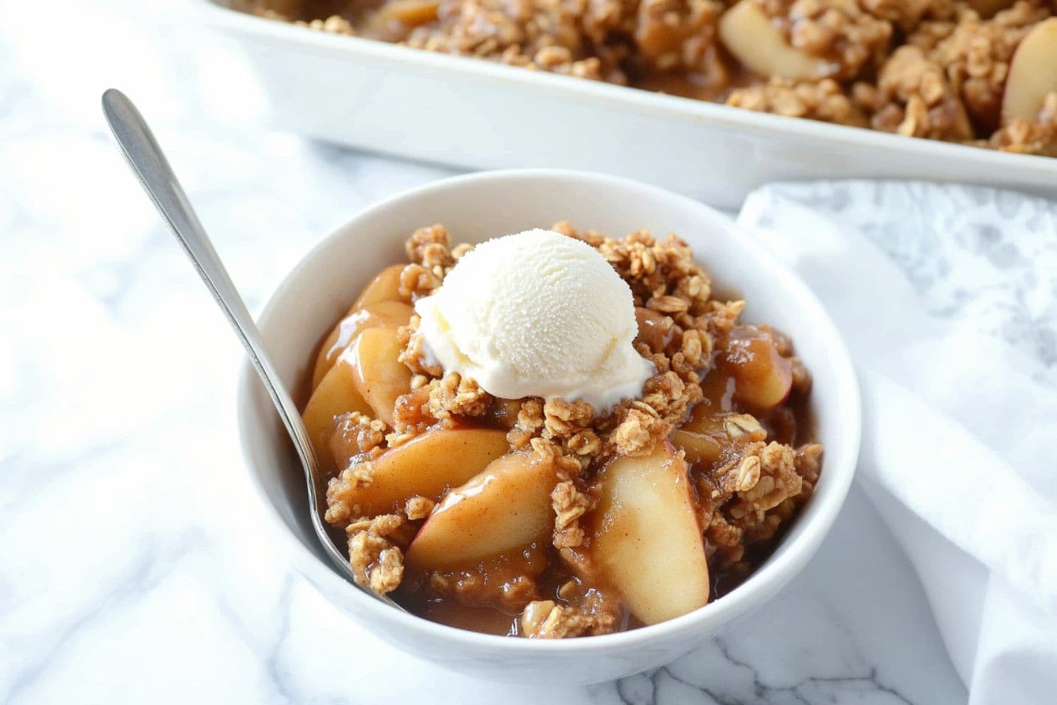 Peanut butter apple crisp with oat topping garnished with vanilla ice cream served in a white bowl.