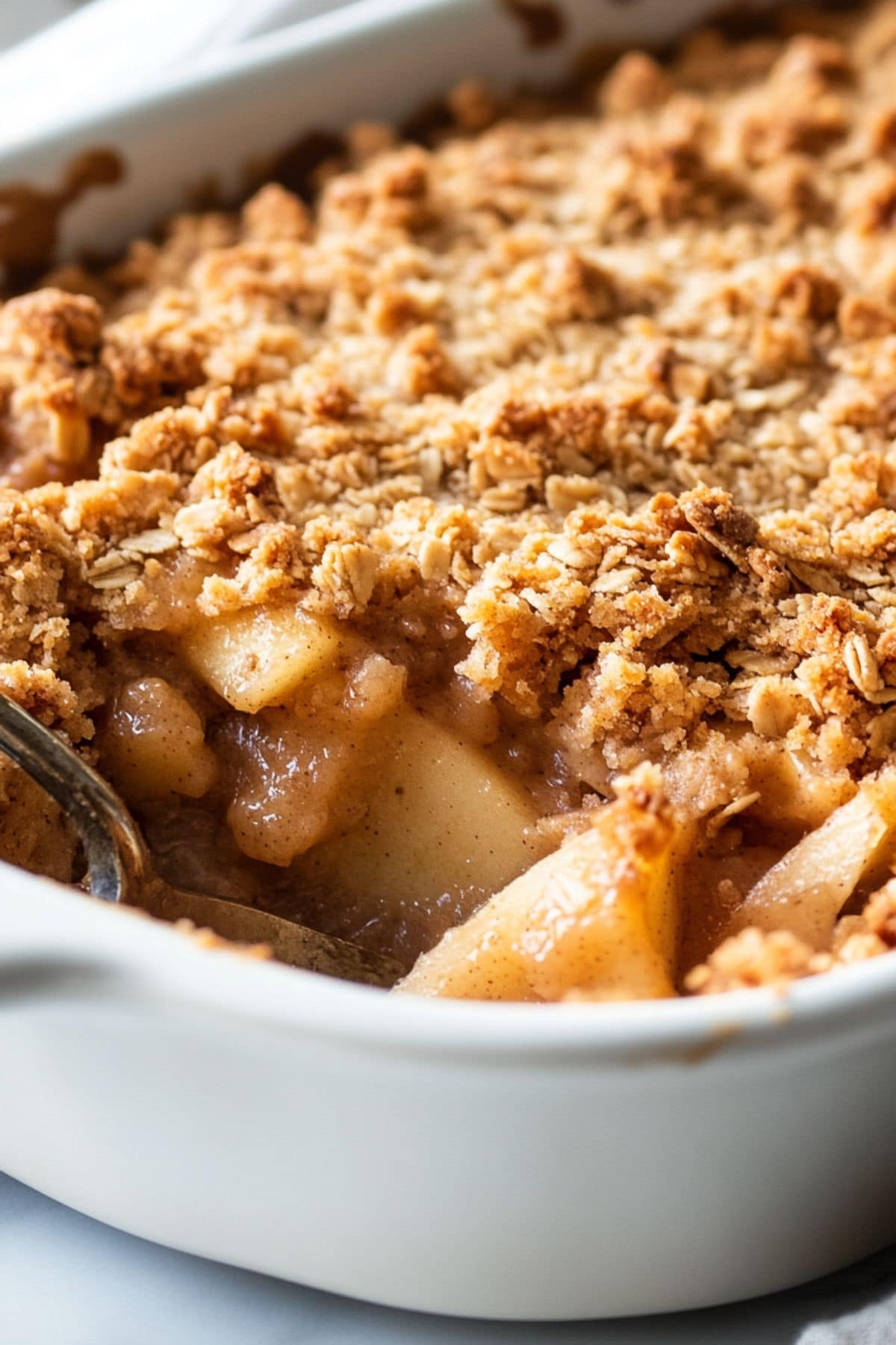 Peanut butter apple crisp in a white baking dish scooped with a spoon.