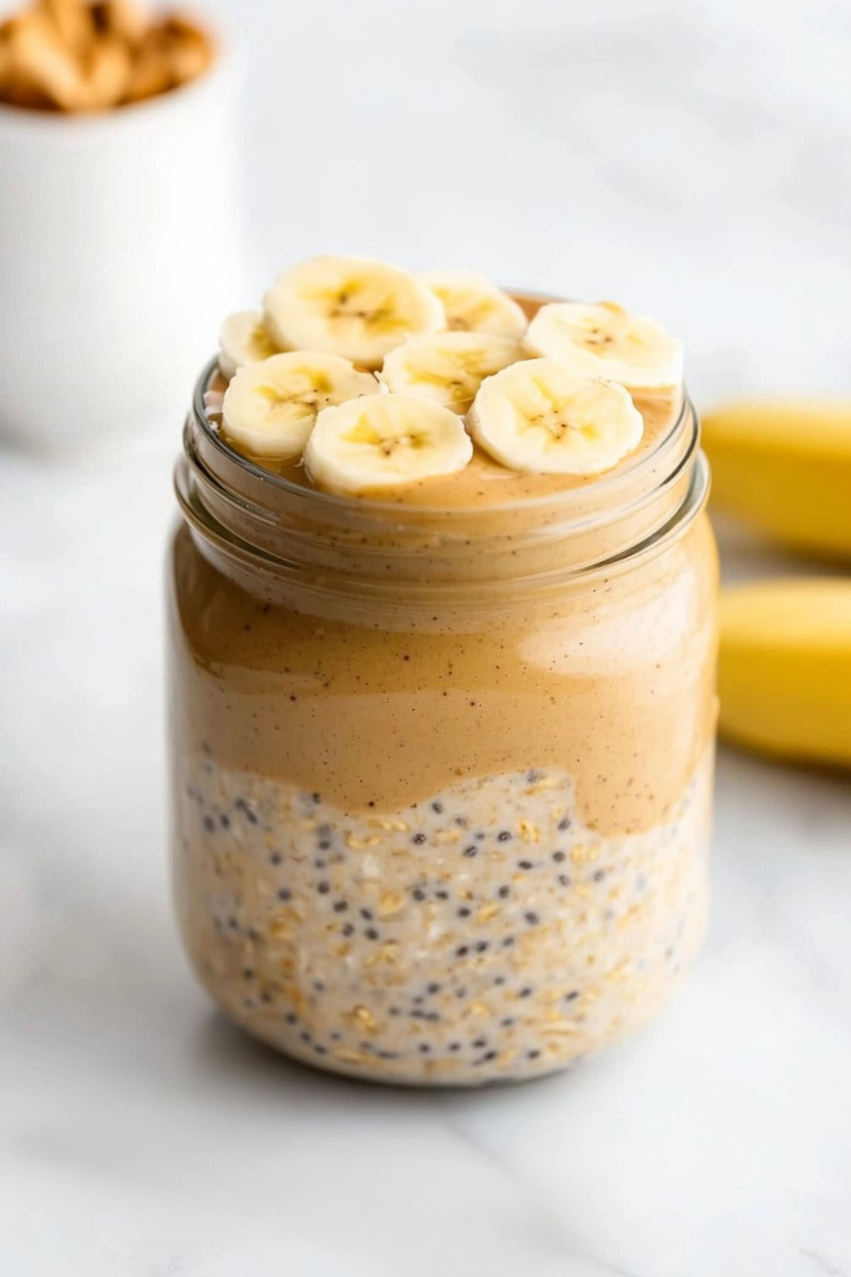 Peanut butter overnight oats served in a clear jar, garnished with sliced bananas.