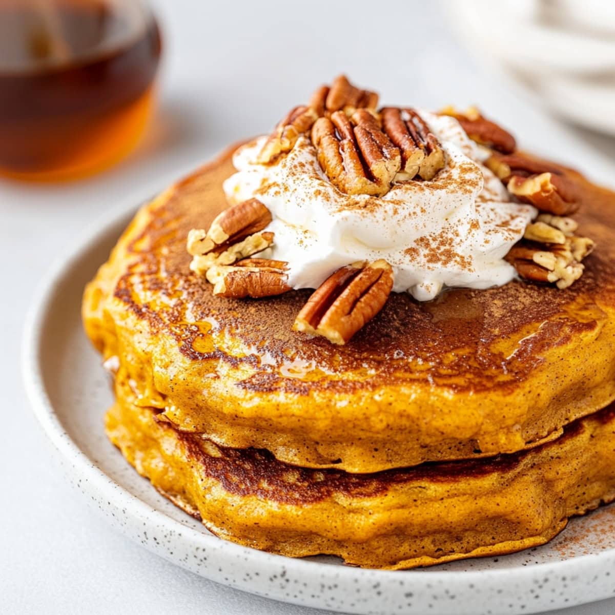 Homemade pumpkin spice pancakes topped with whipped cream and nuts.