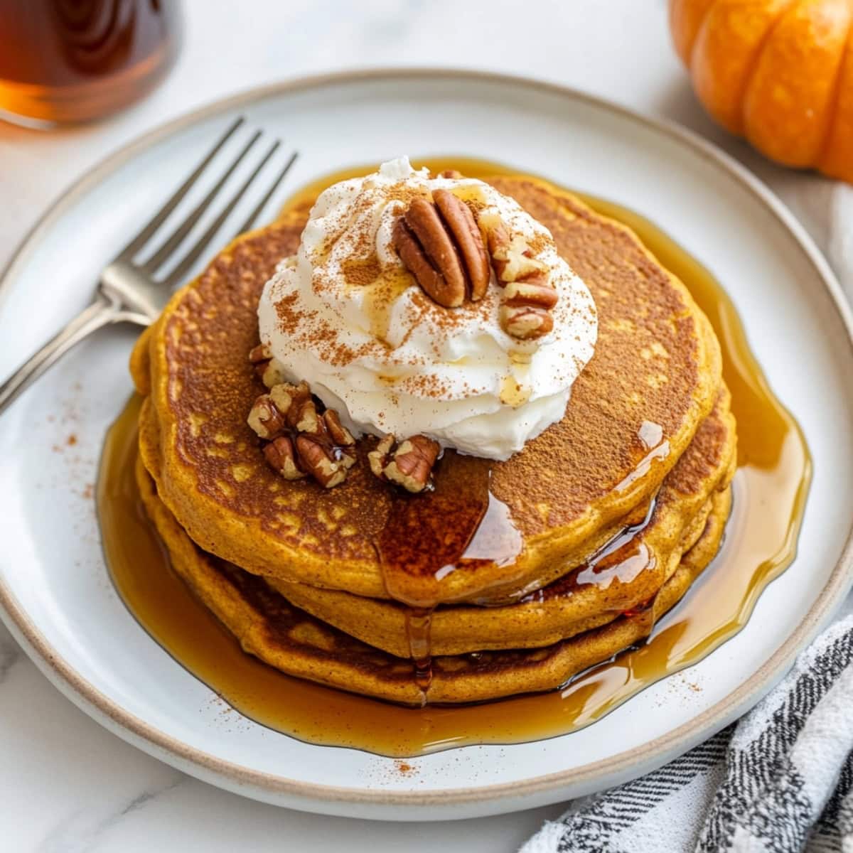 Pumpkin spice pancakes served with whipped cream and a dusting of nutmeg on a plate, top view