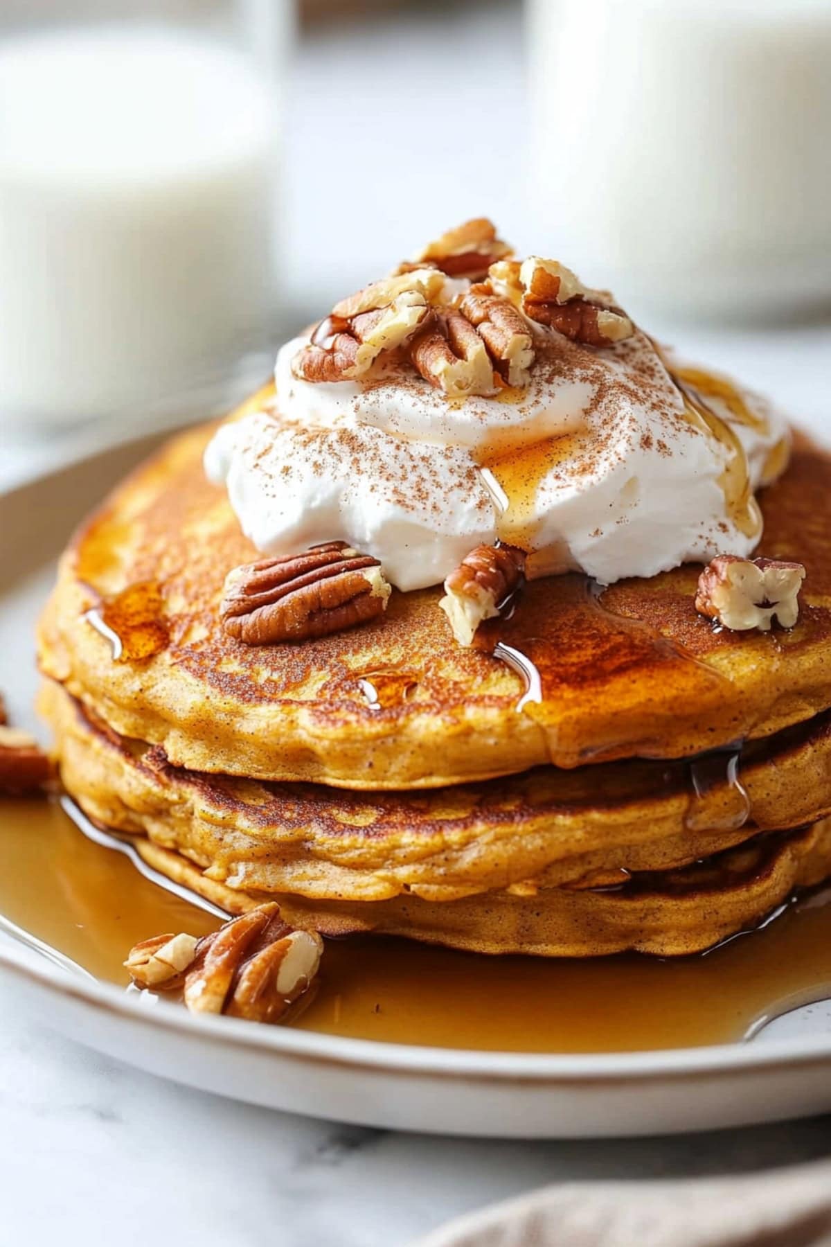 Three pumpkin spice pancakes stacked on a white plate with whipped cream and pecans