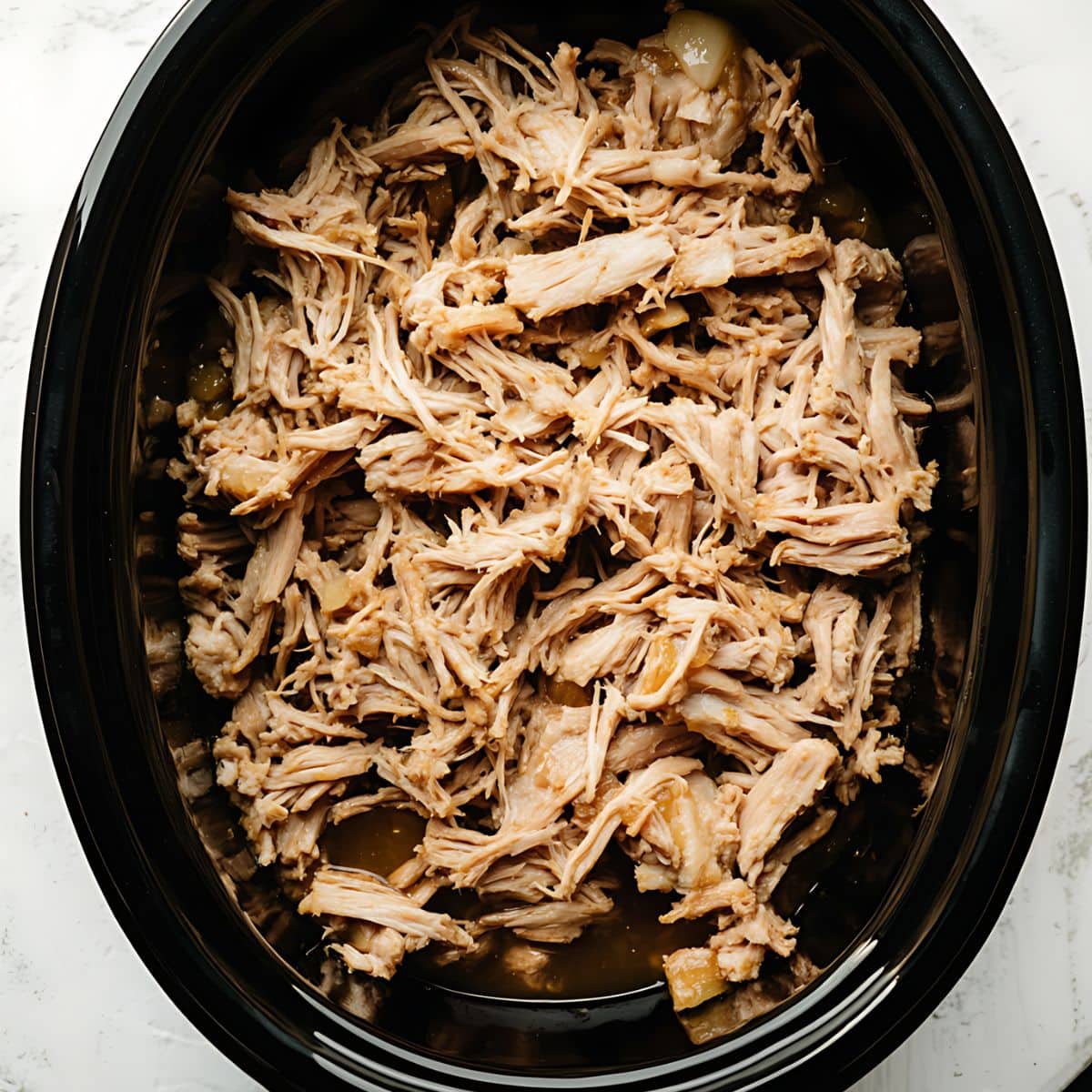 Pulled pork with apple cider sauce cooked inside a slow cooker.