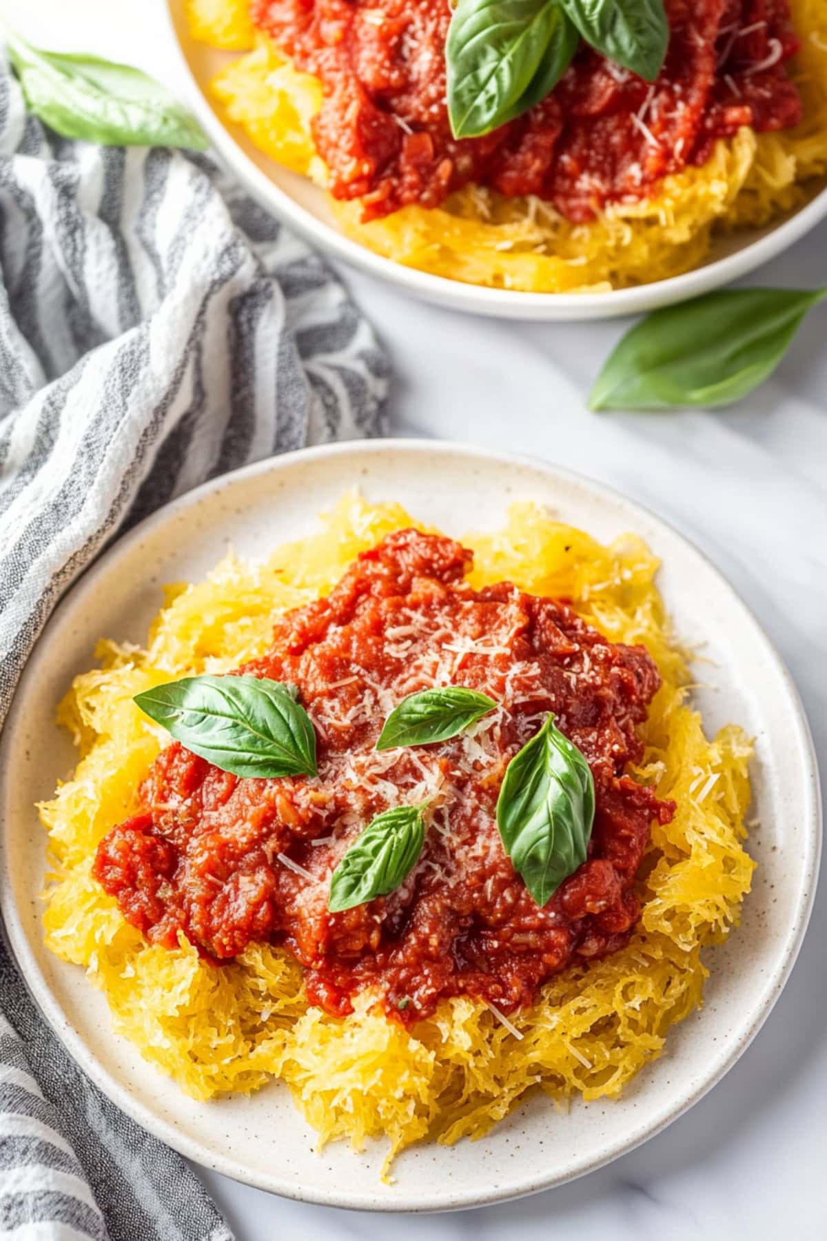 A plate of spaghetti squash with marinara sauce, basil and grated parmesan.