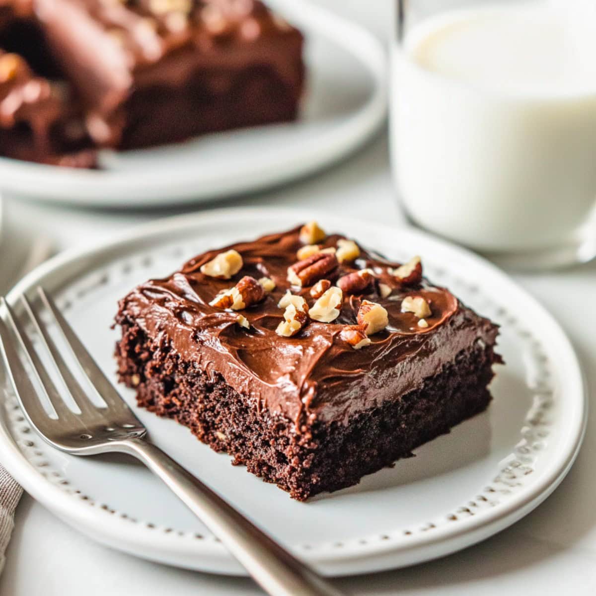 A piece of fudgy Texas sheet cake brownie on a white plate, served with milk.