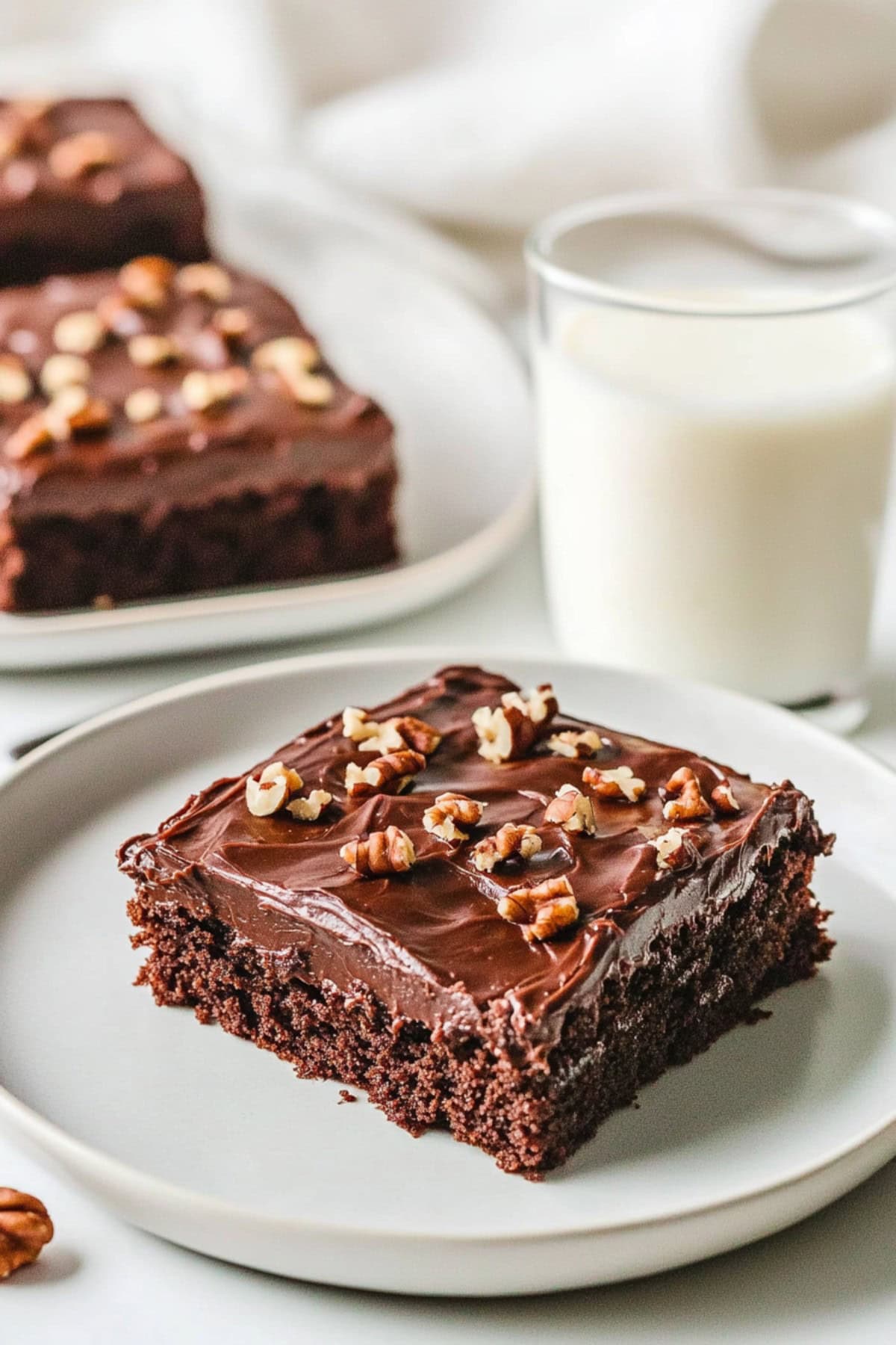 Texas sheet cake brownie slice on a white plate topped with chopped walnuts, served with milk.