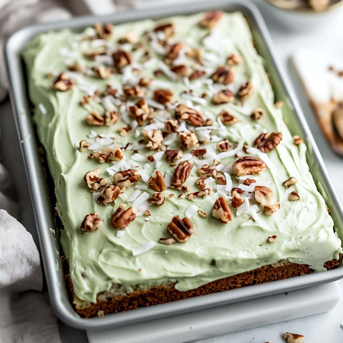 Watergate cake with green frosting, chopped pecans and shredded coconut in a  baking pan.