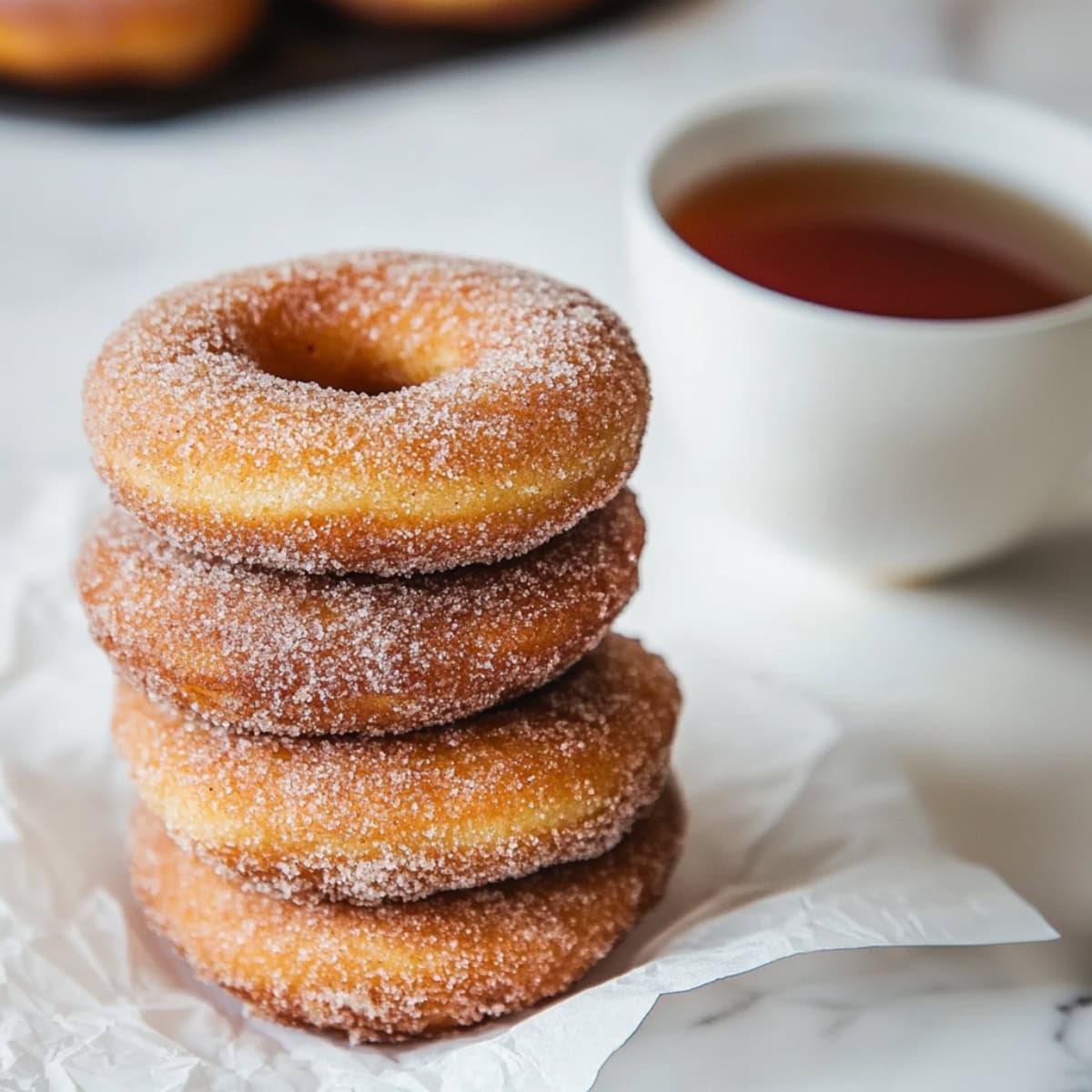 Cinnamon coated sugar Baked Apple Cider Donuts stacked next to a cup of tea