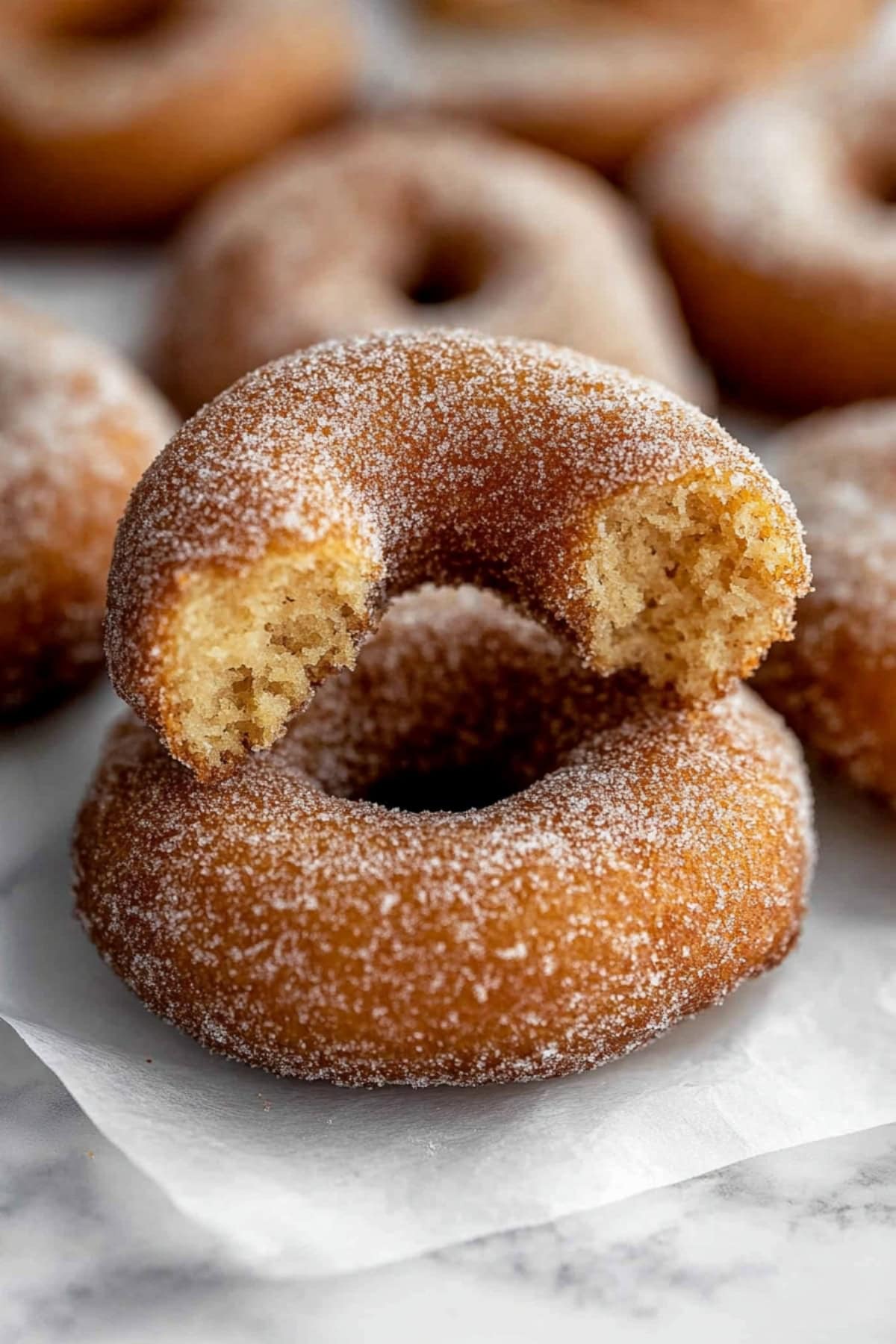 Donut cut into half on top of a whole donut lying on a parchment paper, close up