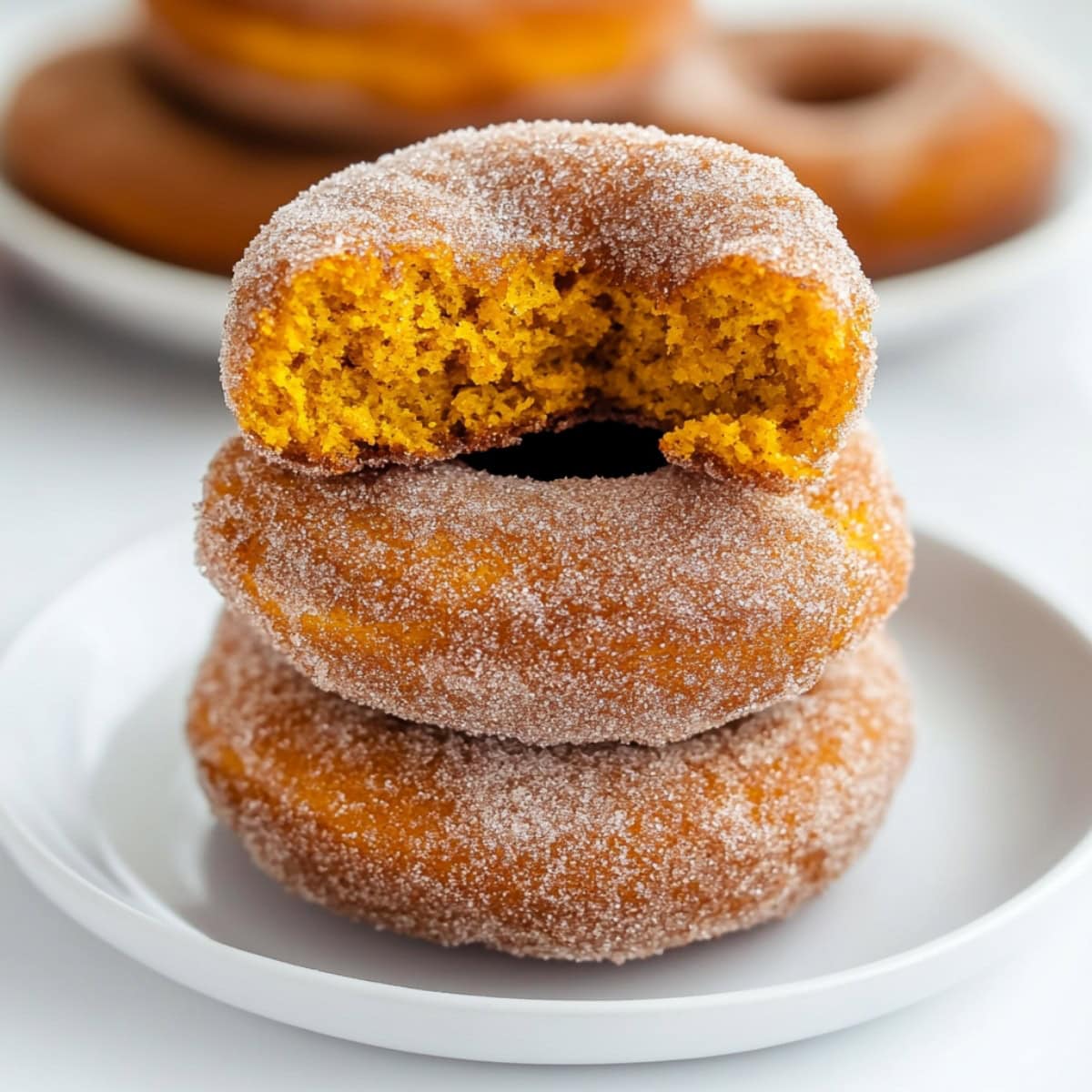 Cinnamon sugar coated pumpkin donuts stacked don a white plate, side view