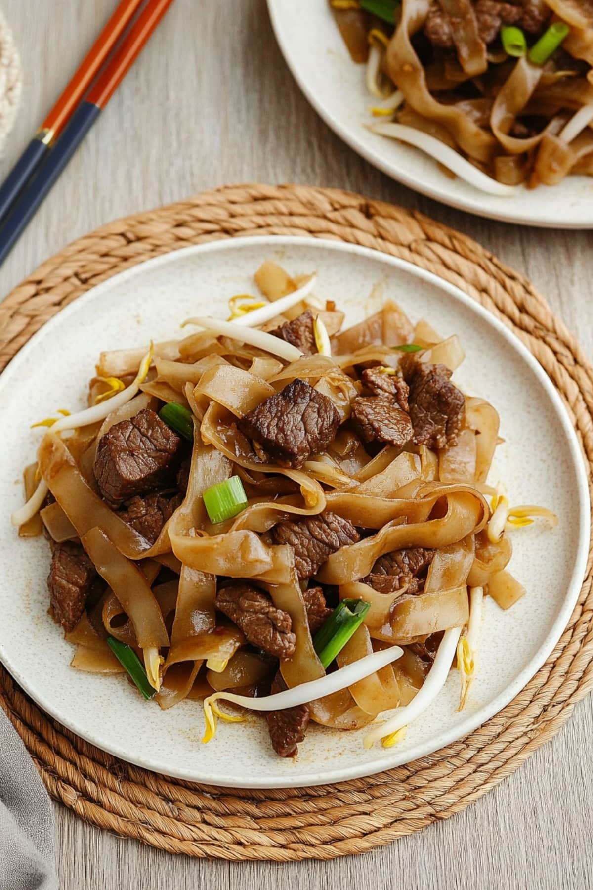 Two plate on top of a wooden table with servings of beef chow fun.