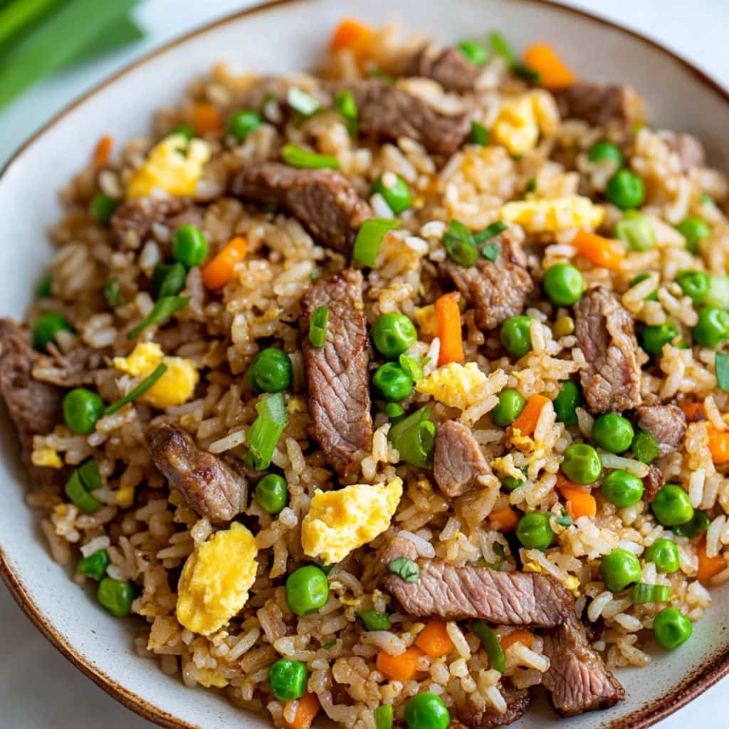 Beef fried rice with scrambled eggs, peas and carrots served in a large plate.