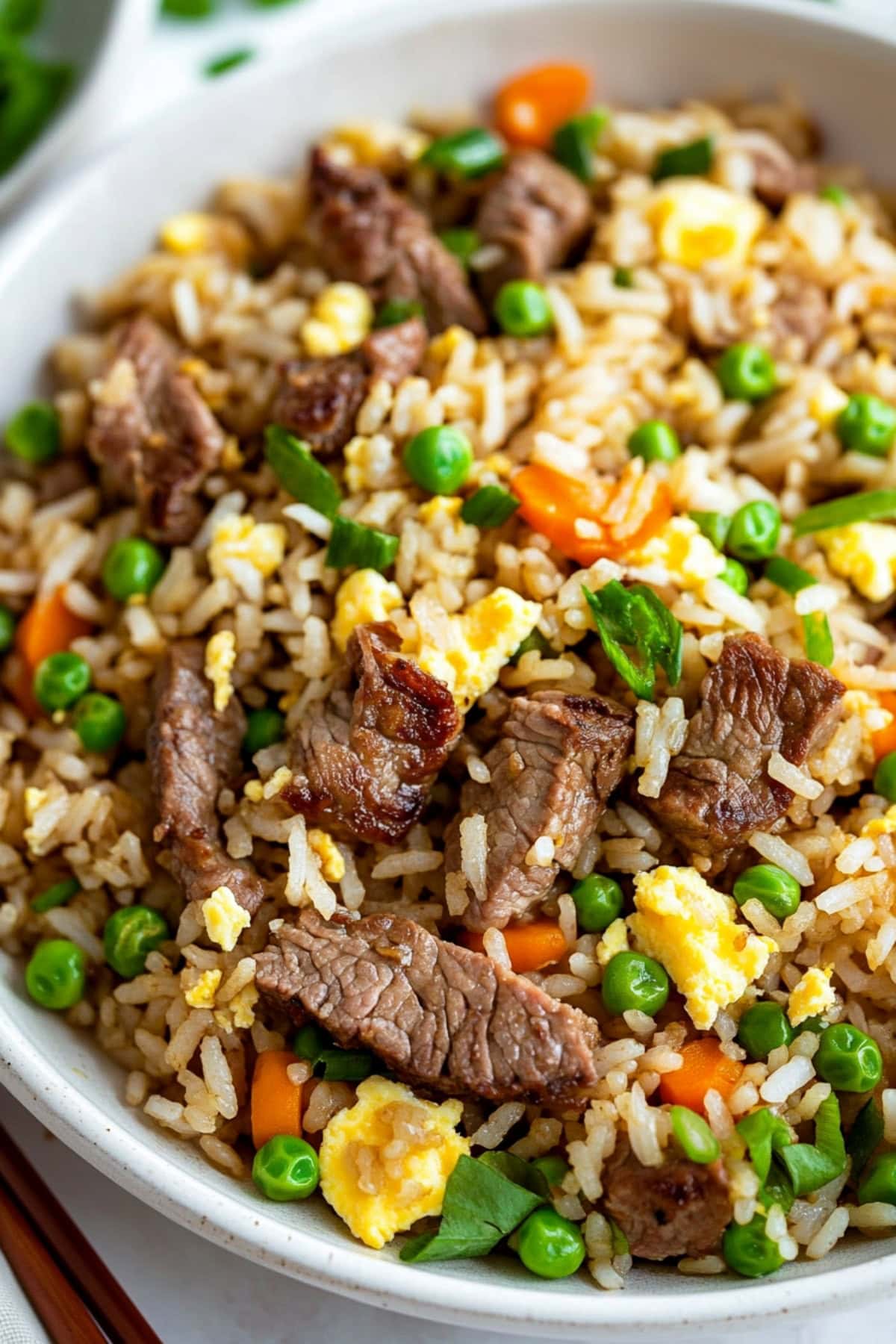 Fried rice with beef, green peas, carrots and eggs served in a white plate.