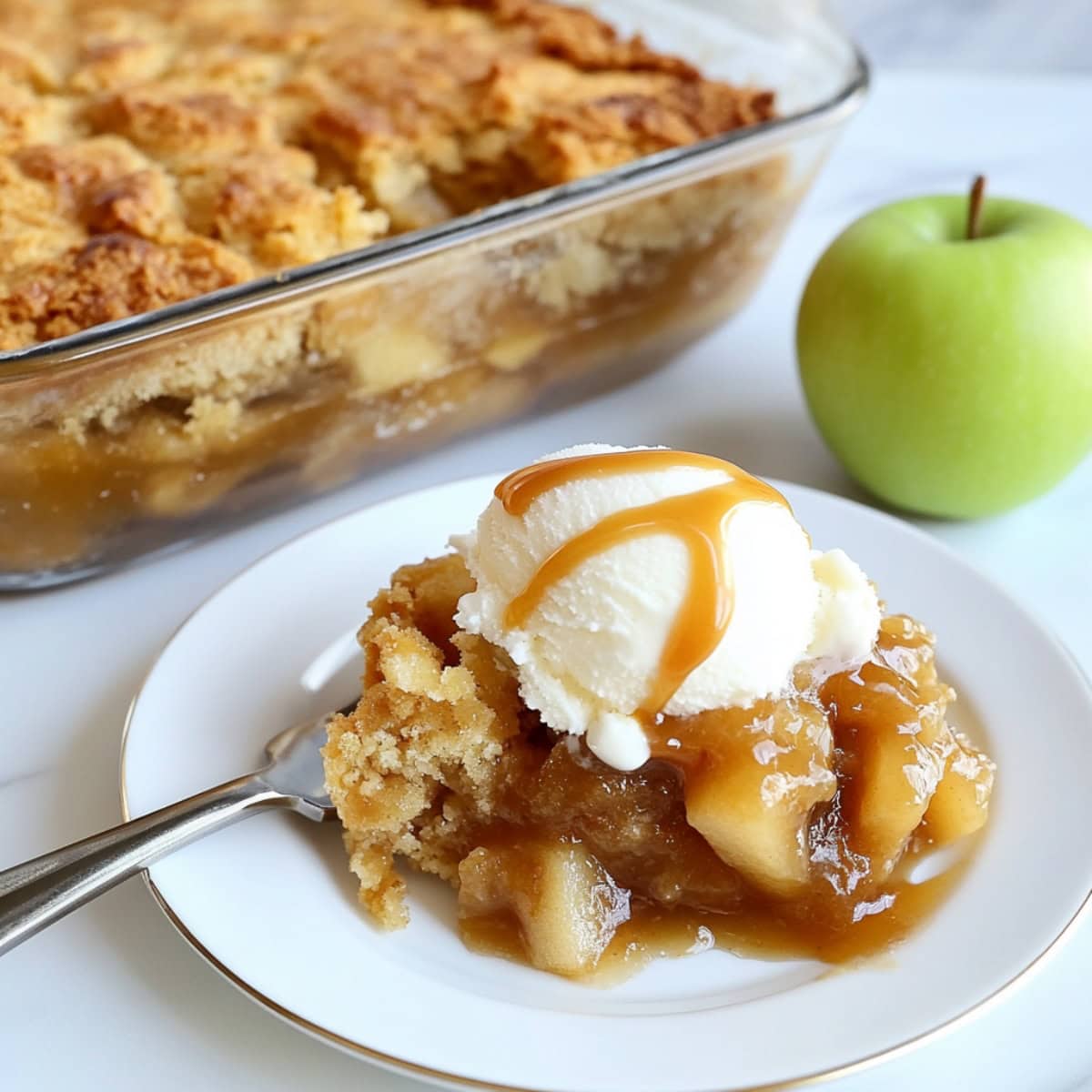 Caramel apple dump cake serving on a white plate garnished with vanilla ice cream.