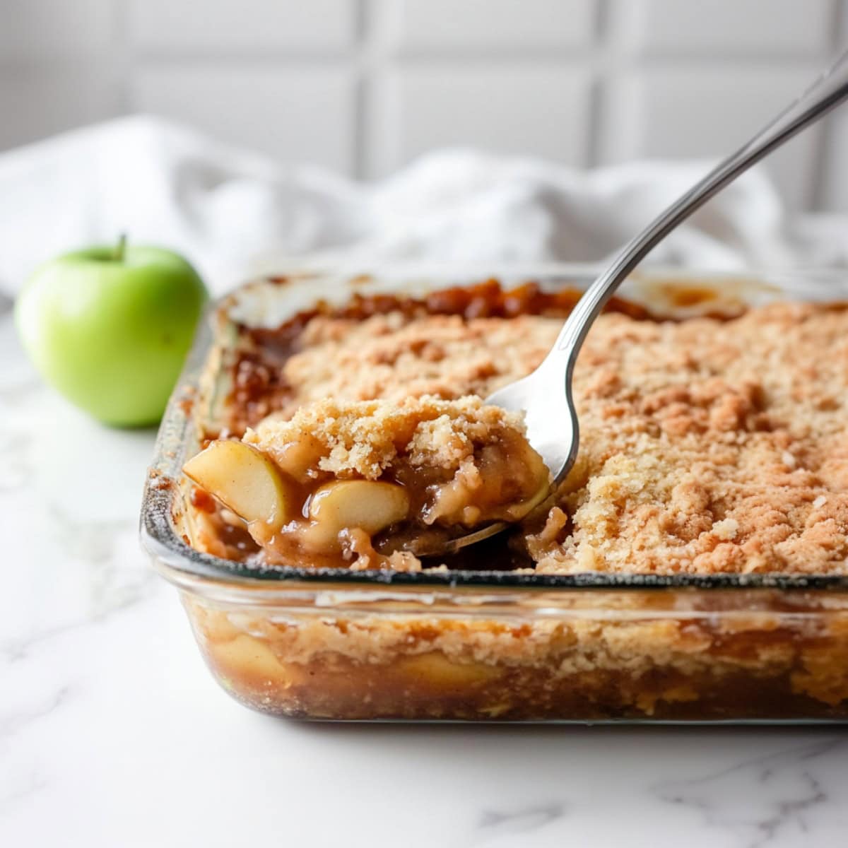 Spoon scooping a portion of caramel apple dump cake from the glass baking dish, side view