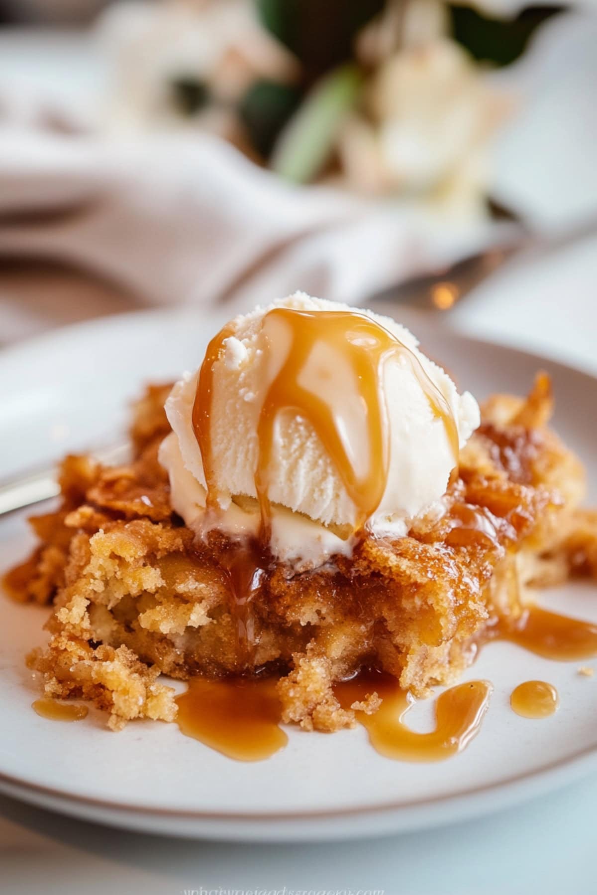 Serving of caramel apple cake with scoop of vanilla ice cream served on a white plate.