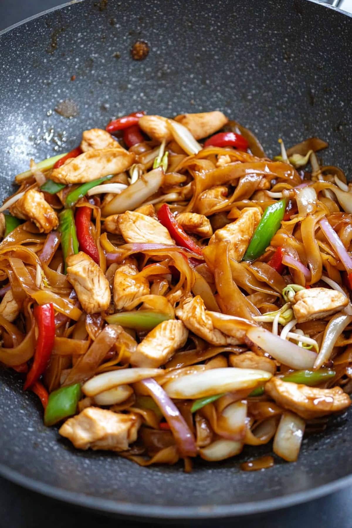 A wok filled with chicken chow fun, showing the seared noodles and a medley of vegetables."