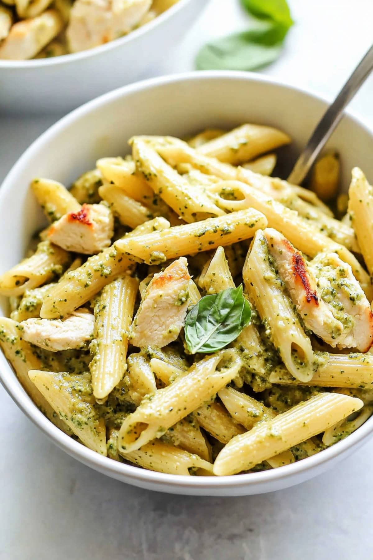 Chicken pesto pasta in a bowl, garnished with basil.