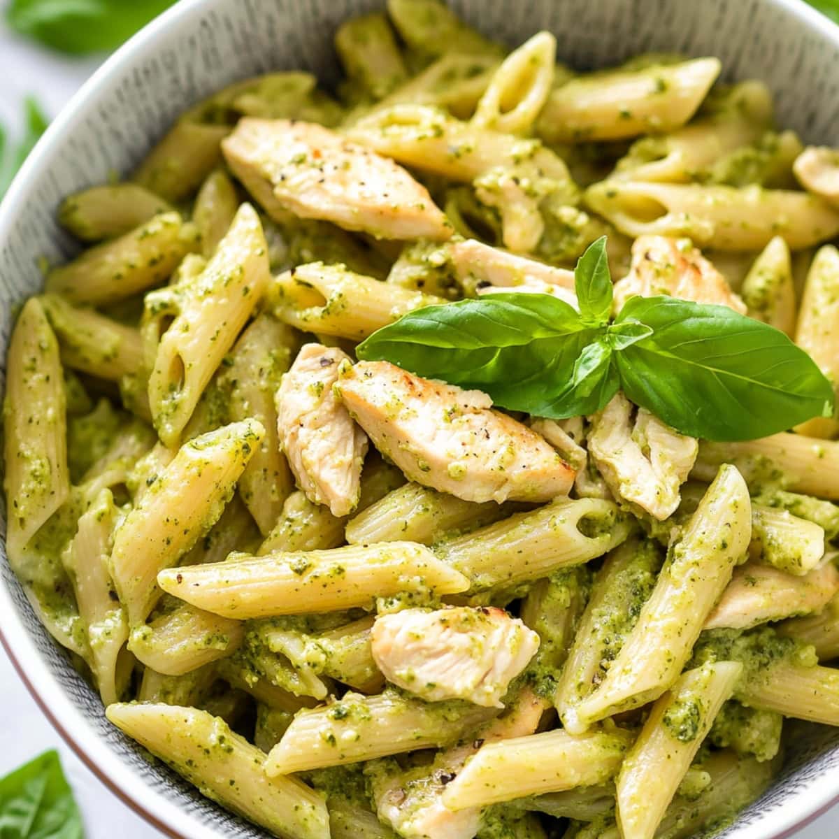 Penne pasta coated in creamy pesto sauce, mixed with juicy chicken pieces in a bowl.