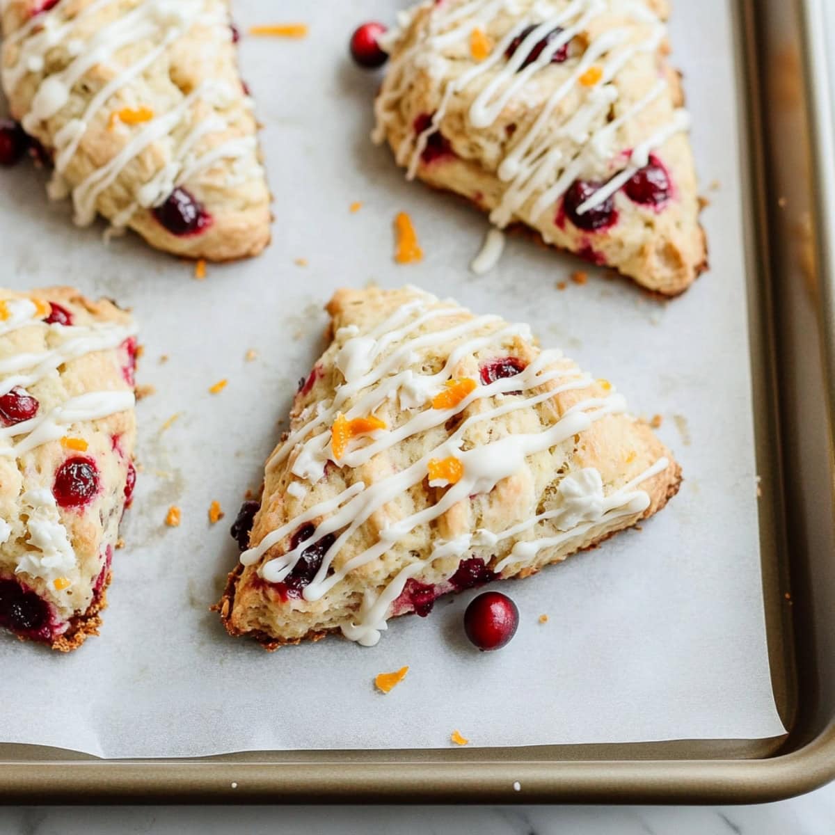 Cranberry orange scones with a light glaze on a baking tray, top view.