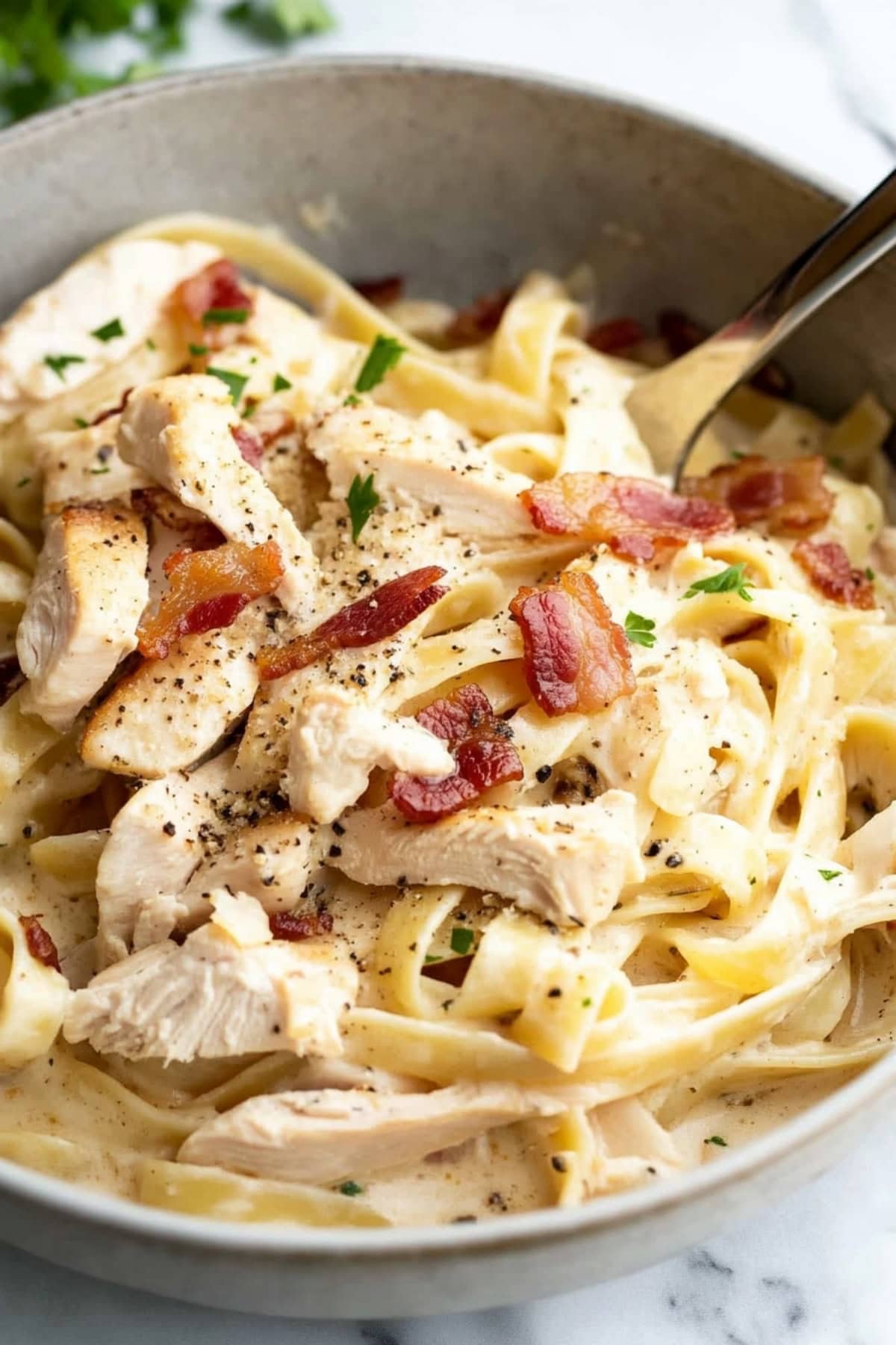 A bowl of creamy chicken and bacon pasta, garnished with herbs, close up