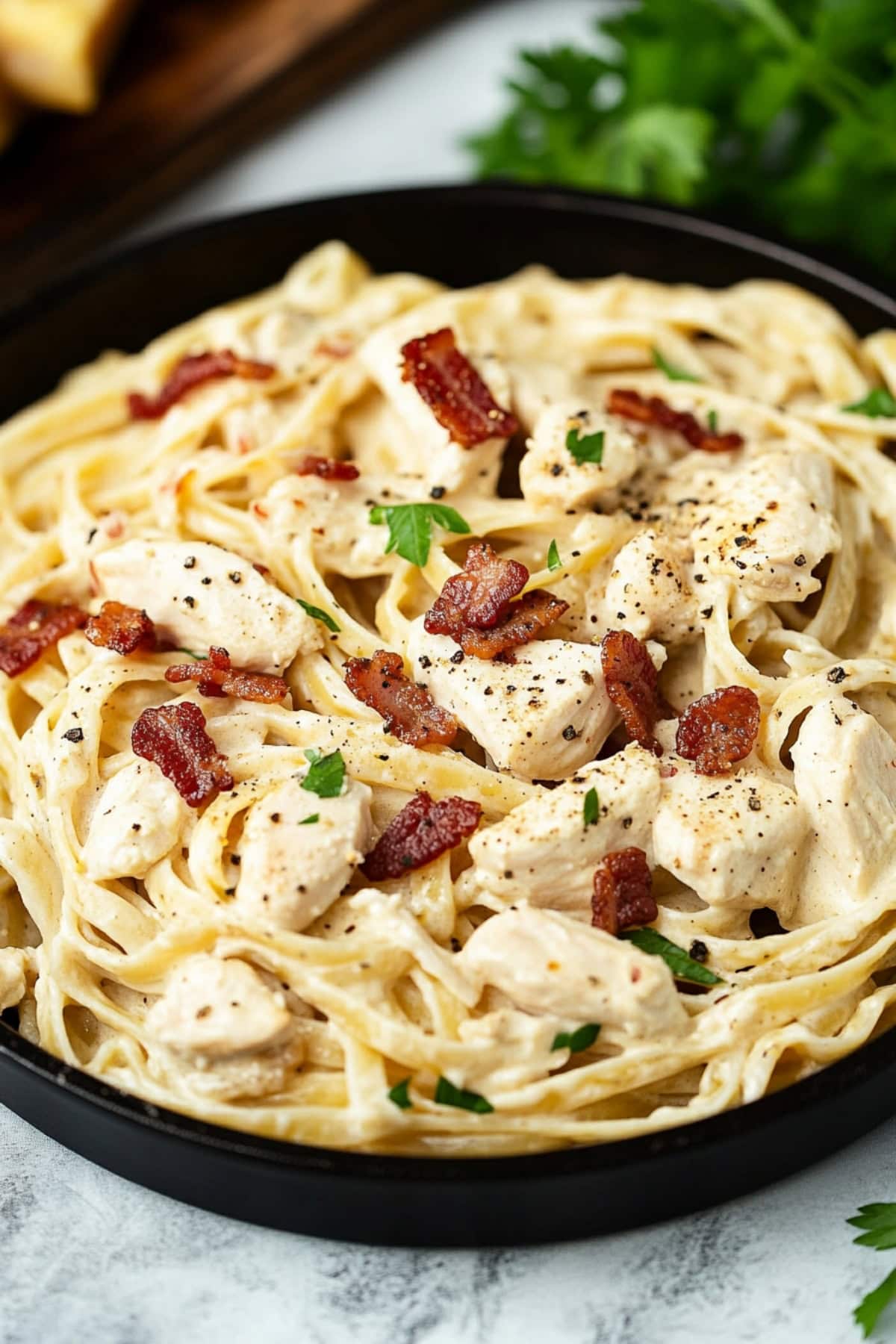 A serving of creamy chicken and bacon pasta in a black skillet.