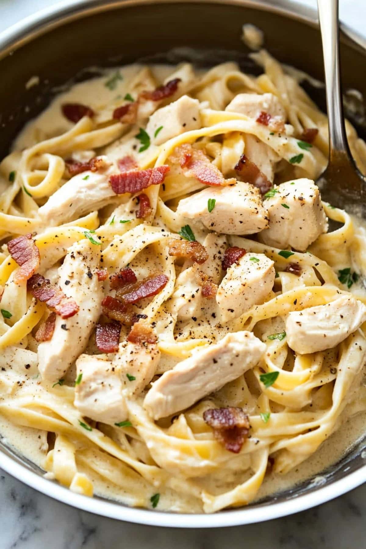 An overhead view of creamy chicken and bacon pasta with salt and ground black pepper, close up