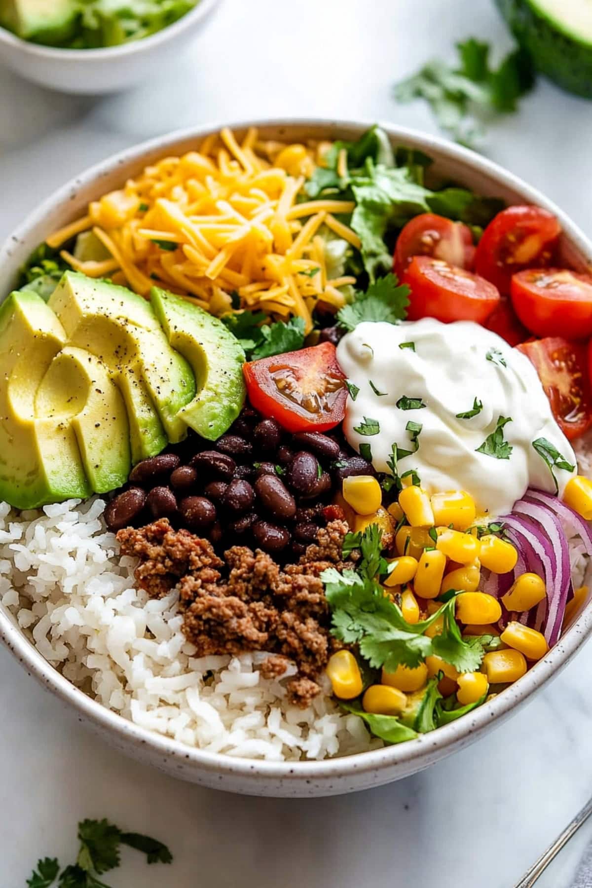 Cilantro lime rice in a white bowl topped with ground beef, black beans, corn and avocado.