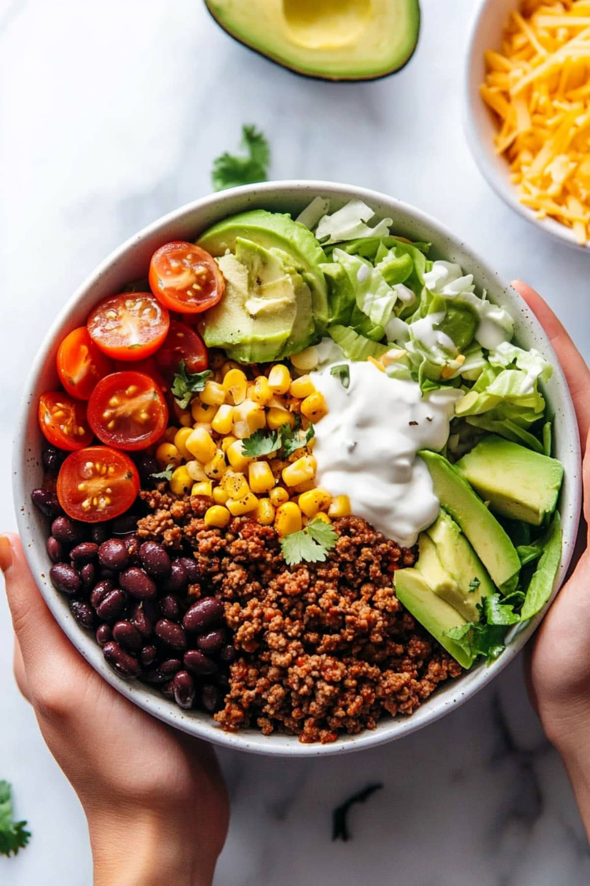 Rice in a white bowl topped with ground beef, cilantro lime rice, black beans, corn and avocado.