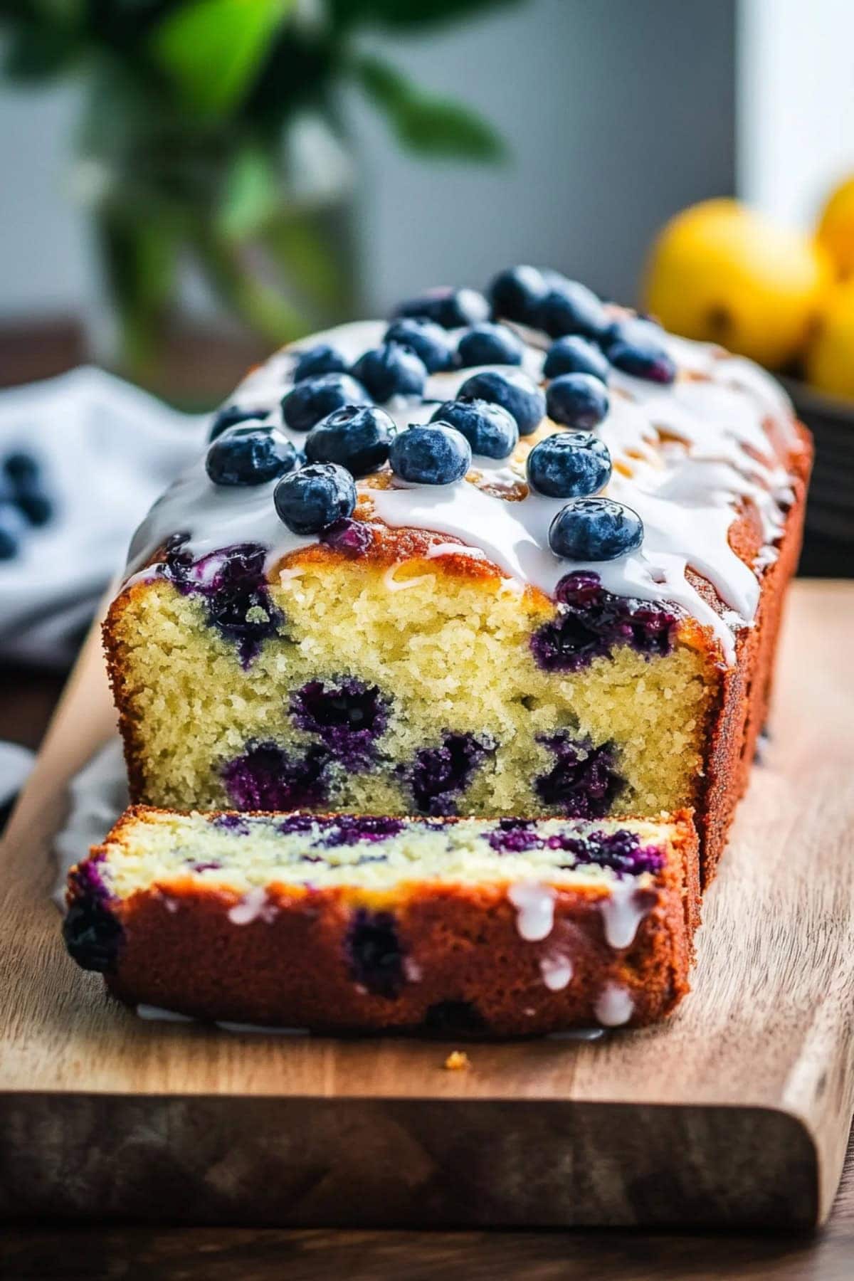 Blueberry yogurt cake with glaze and fresh berries on a wooden board.