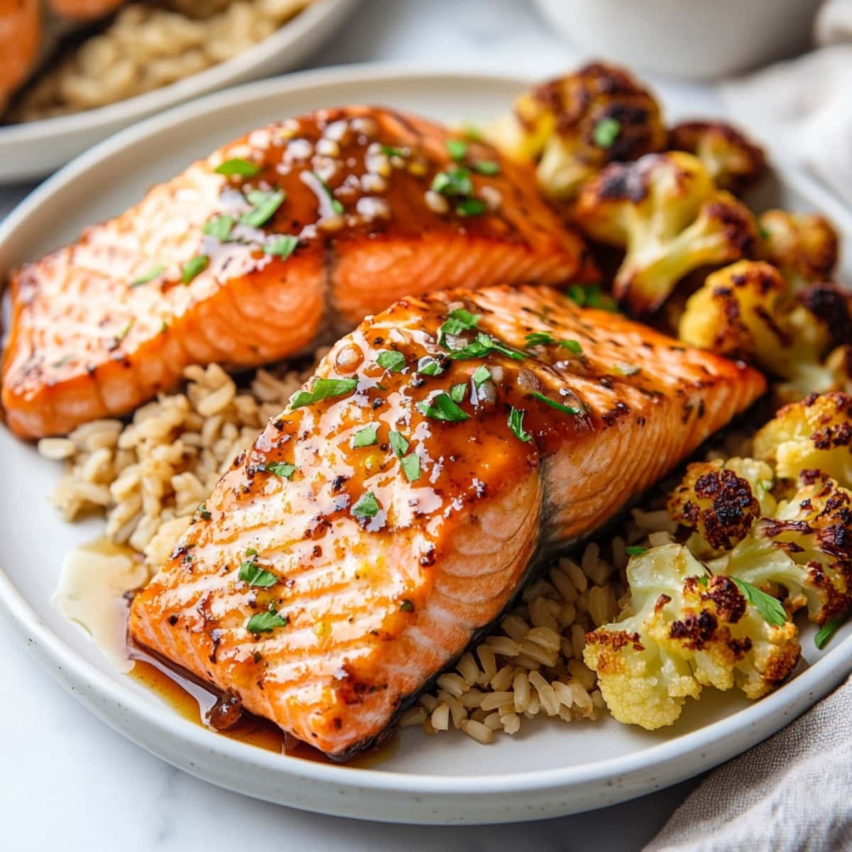 A plate of maple glazed salmon in a bed of wild rice and roasted cauliflower on the side.