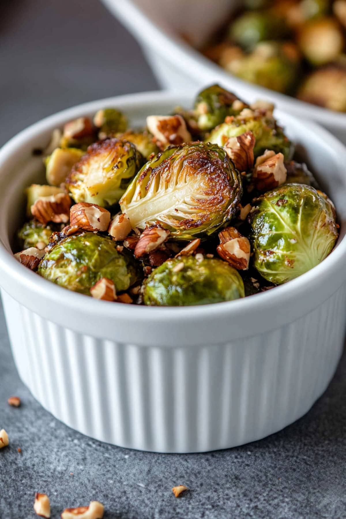 A bowl of maple roasted Brussels sprouts with nuts, their shiny, caramelized surfaces reflecting the warm light.