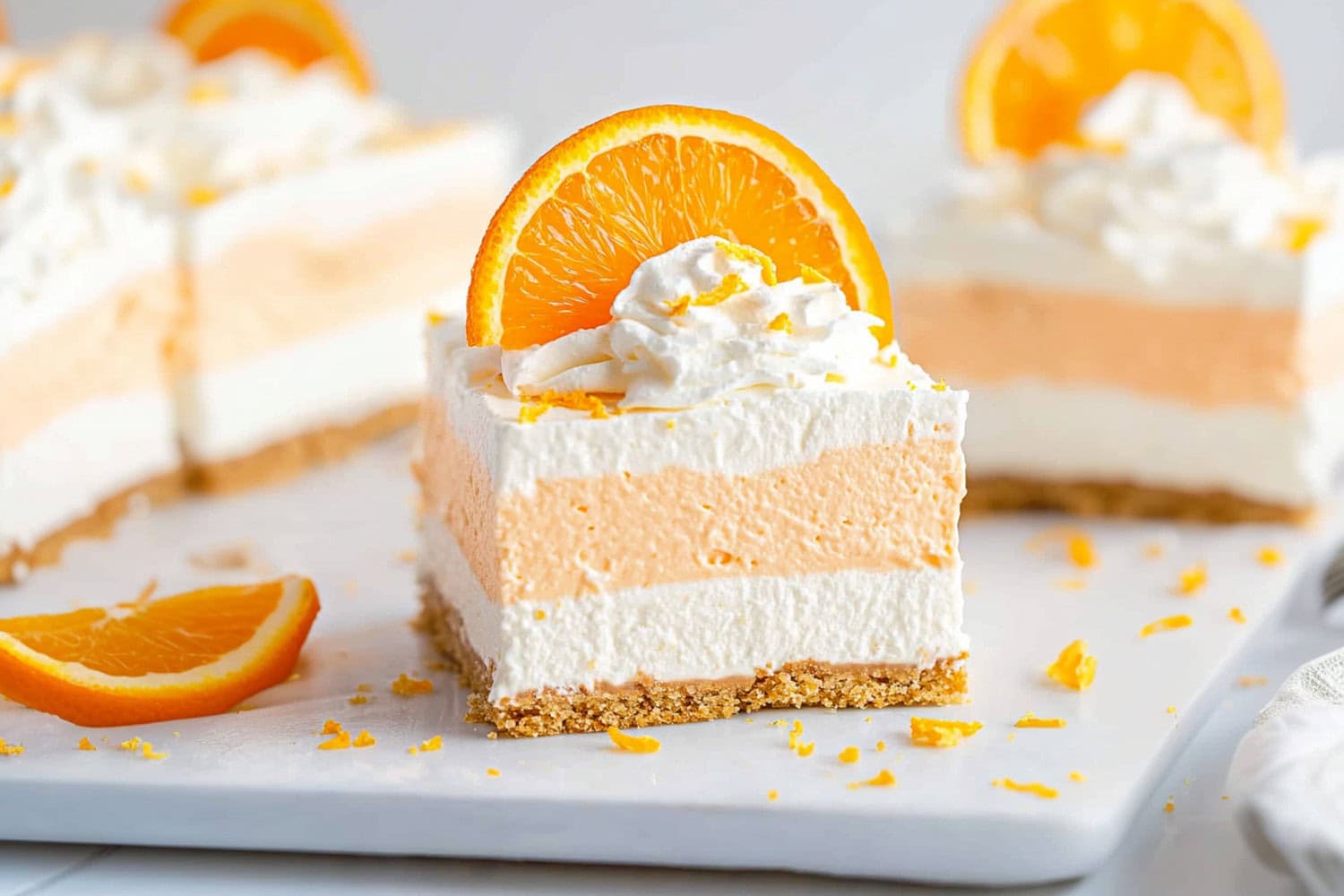 A tray of orange creamsicle dream bars, each square perfectly cut to display the orange and vanilla layers.