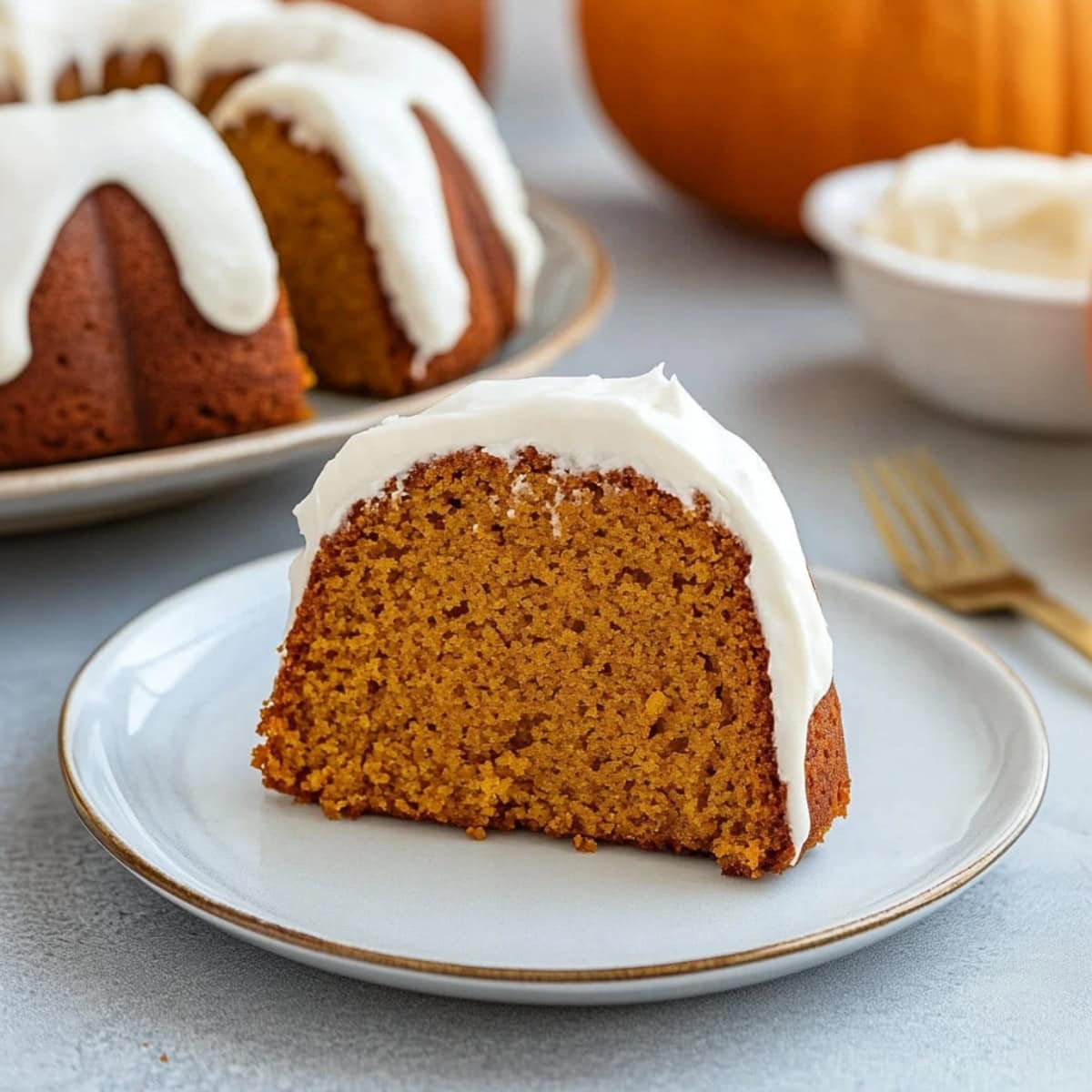 A slice of pumpkin bundt cake served on a white plate with cream cheese frosting on top