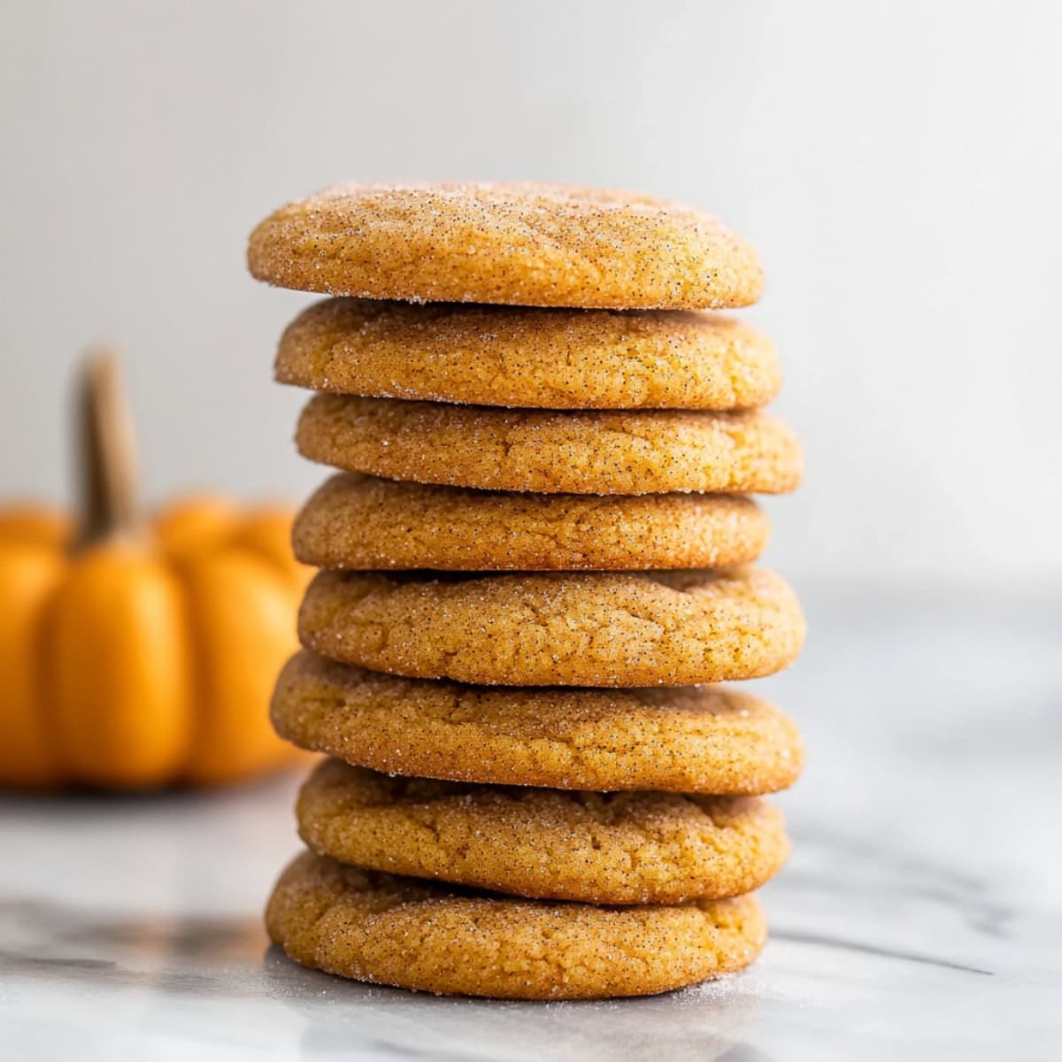 Soft and chewy pumpkin snickerdoodle cookies stacked on a marble table