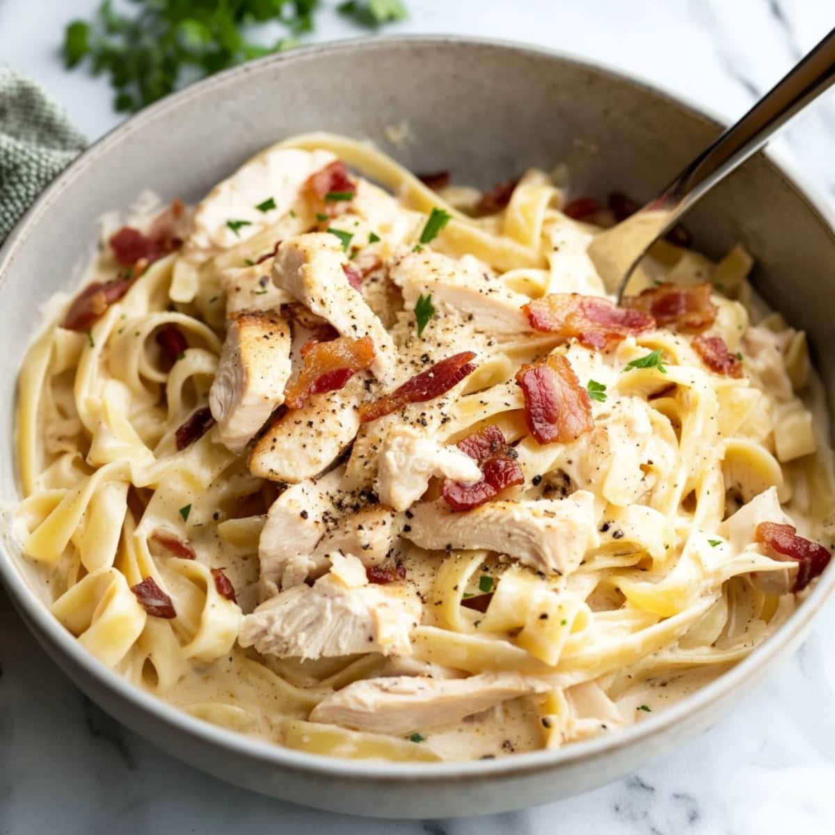 A bowl of creamy chicken and bacon pasta with fettuccine noodles, sprinkled with salt and pepper.