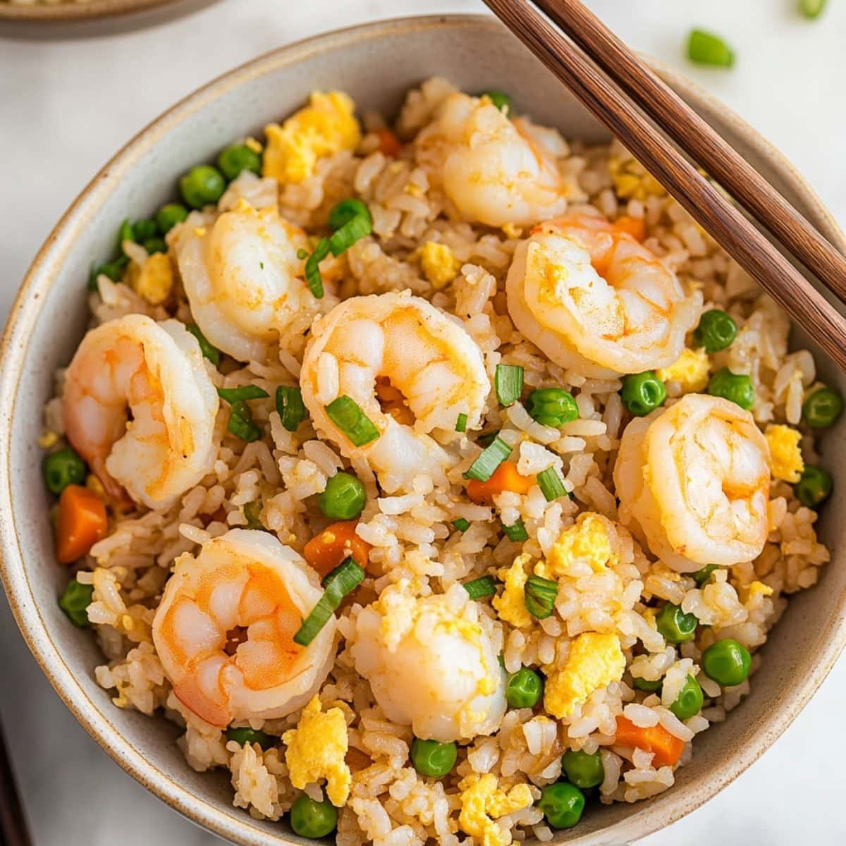 An overhead view of shrimp fried rice with veggies and herbs in a bowl.